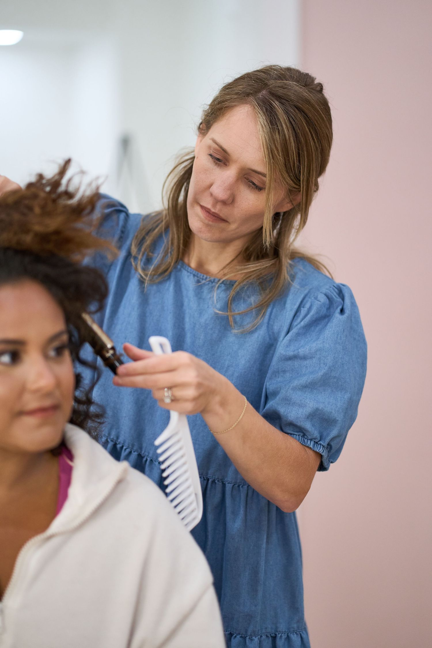 Hair stylist in denim working on styling a client's curly hair.