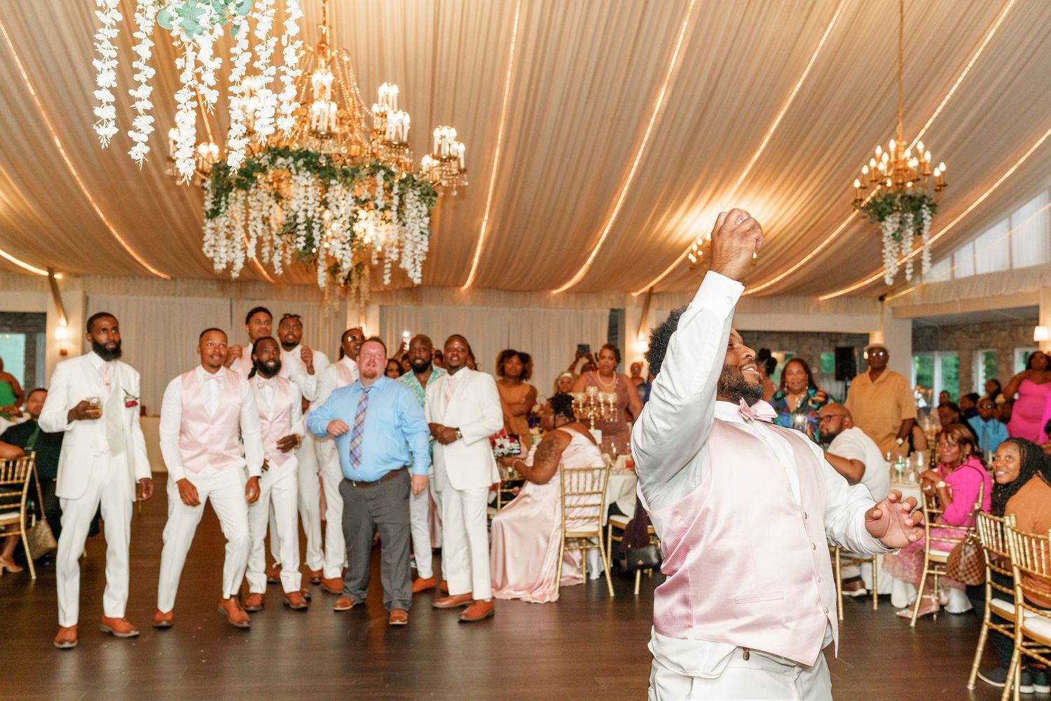 Dynamic dance moves under elegant chandeliers at wedding reception with draped ceiling decor.