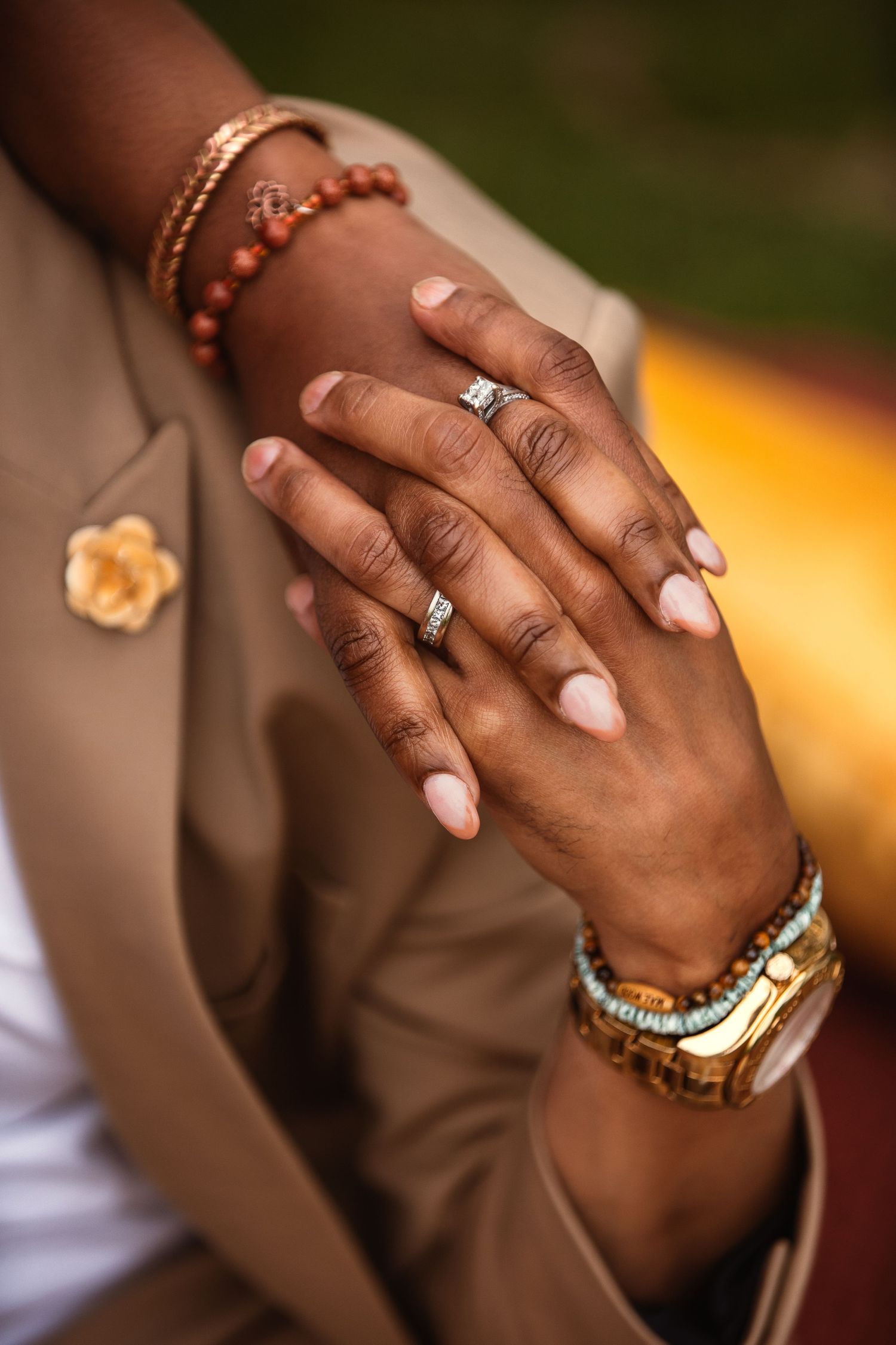 Close-up of elegant hands wearing engagement ring, bracelets and nude nail polish against warm background.