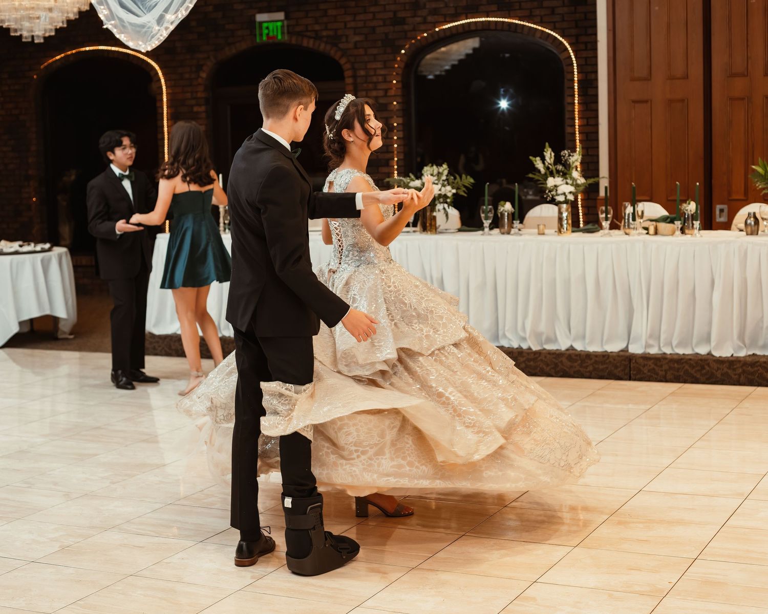 A couple dances together on their wedding day in a beautifully decorated reception hall with brick walls.