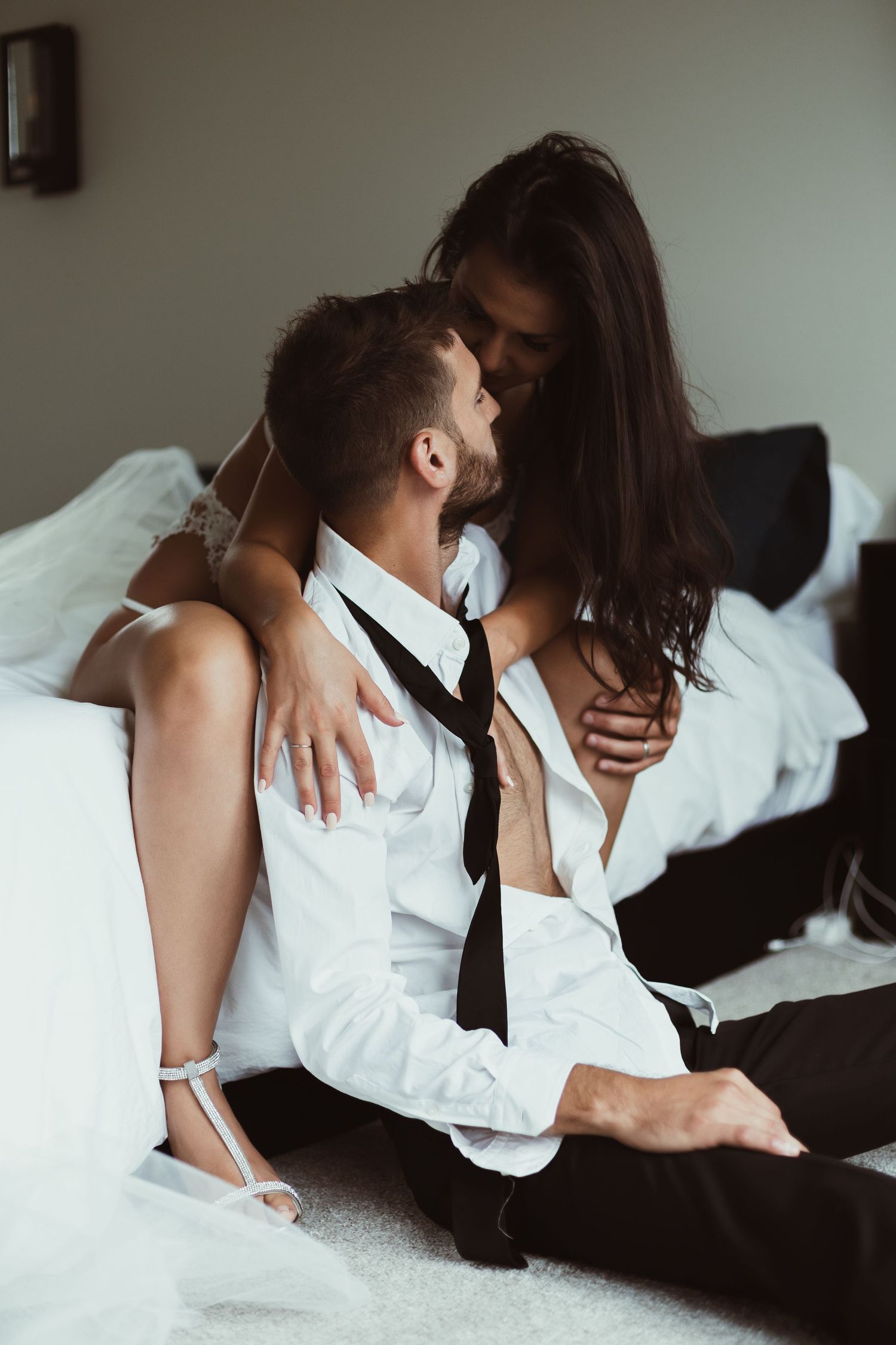 Sensual monochrome portrait of couple embracing on white bedding.