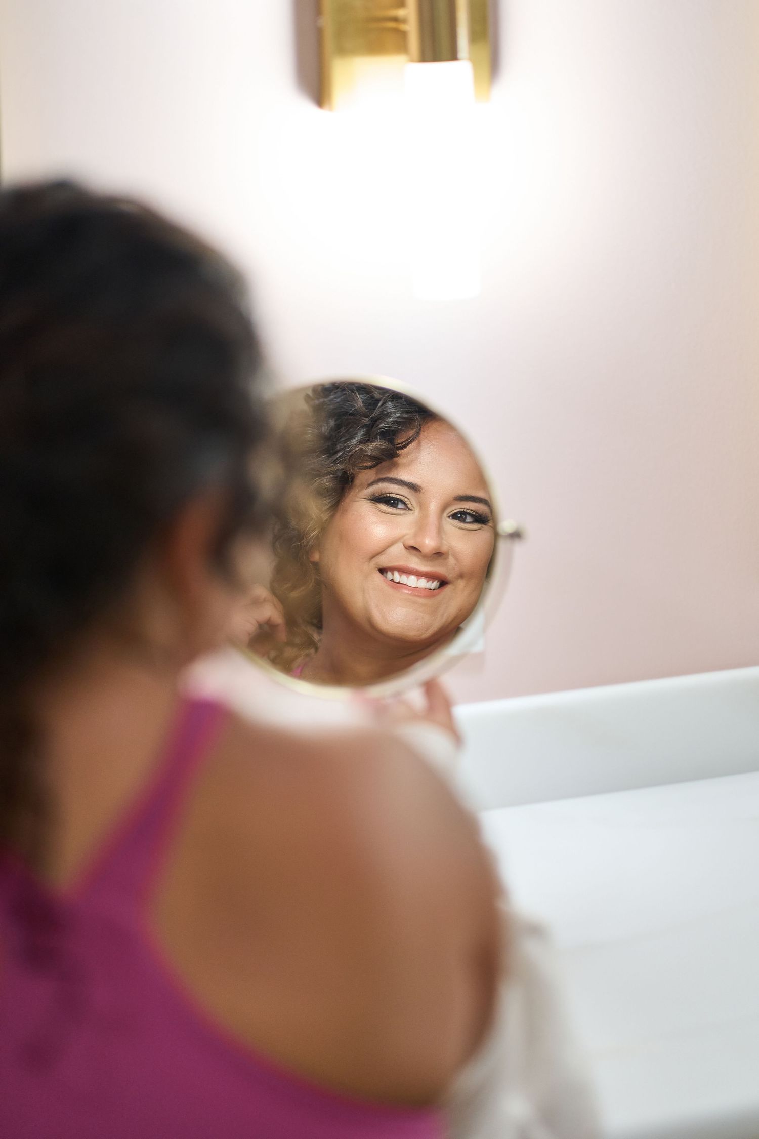 A reflection in a mirror shows a warm smile and elegant bridal makeup.