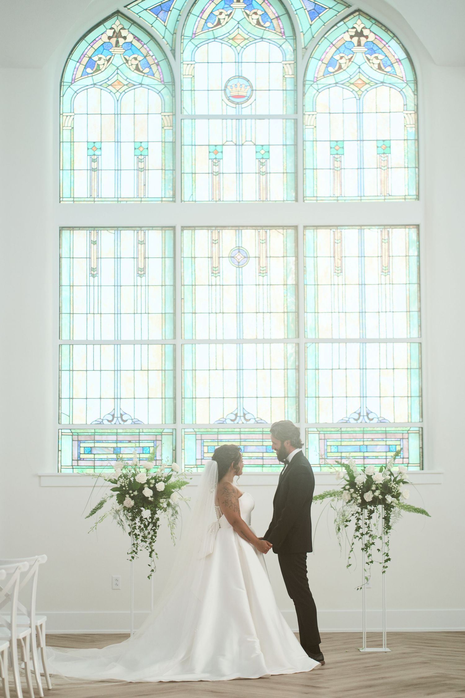 Dreamy bride & groom standing together in front of the cathedral windows in the ceremony area of Kaleidoscope wedding venue in Pierceton, IN