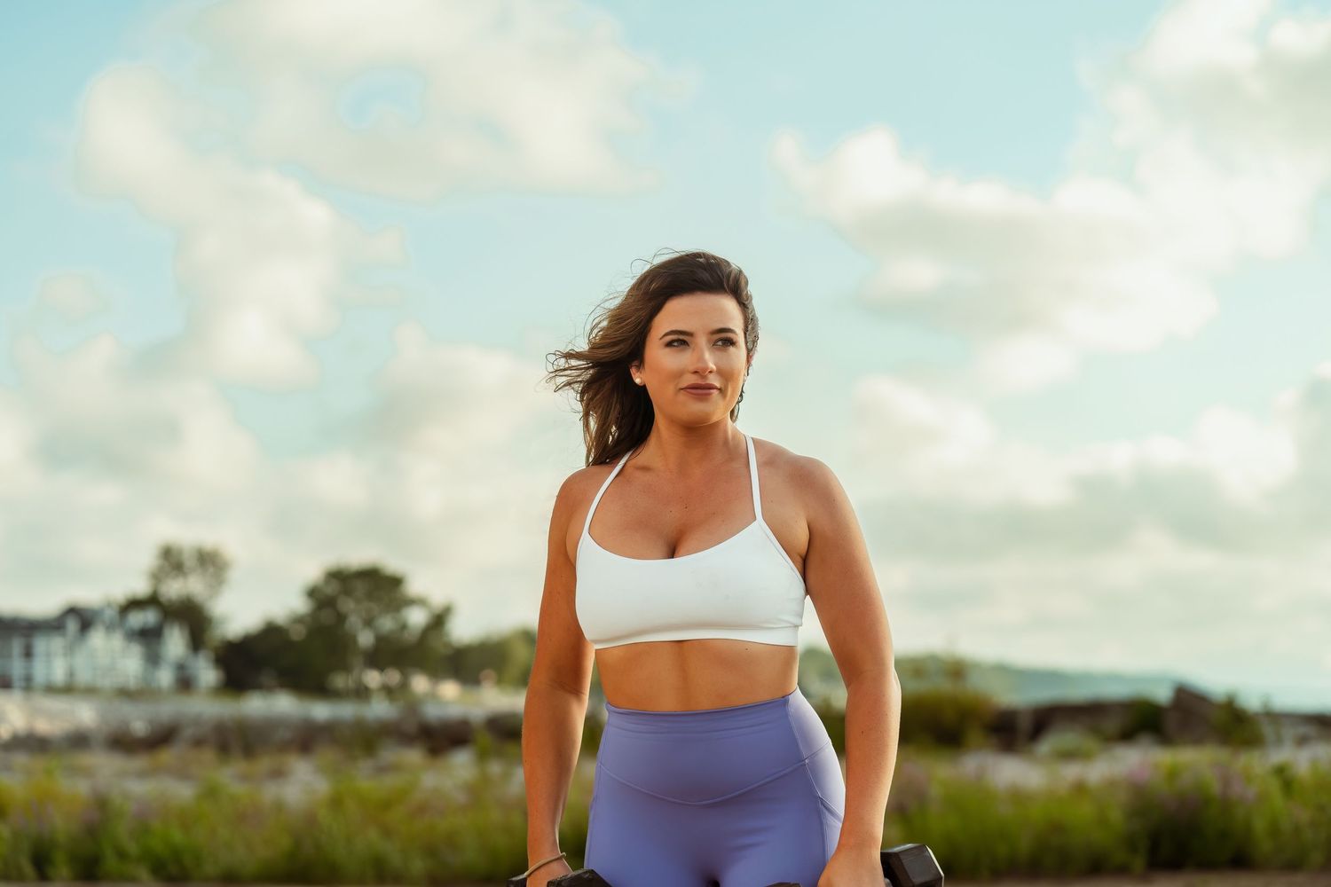 Athletic woman in workout attire poses with dumbbells during beach fitness session.