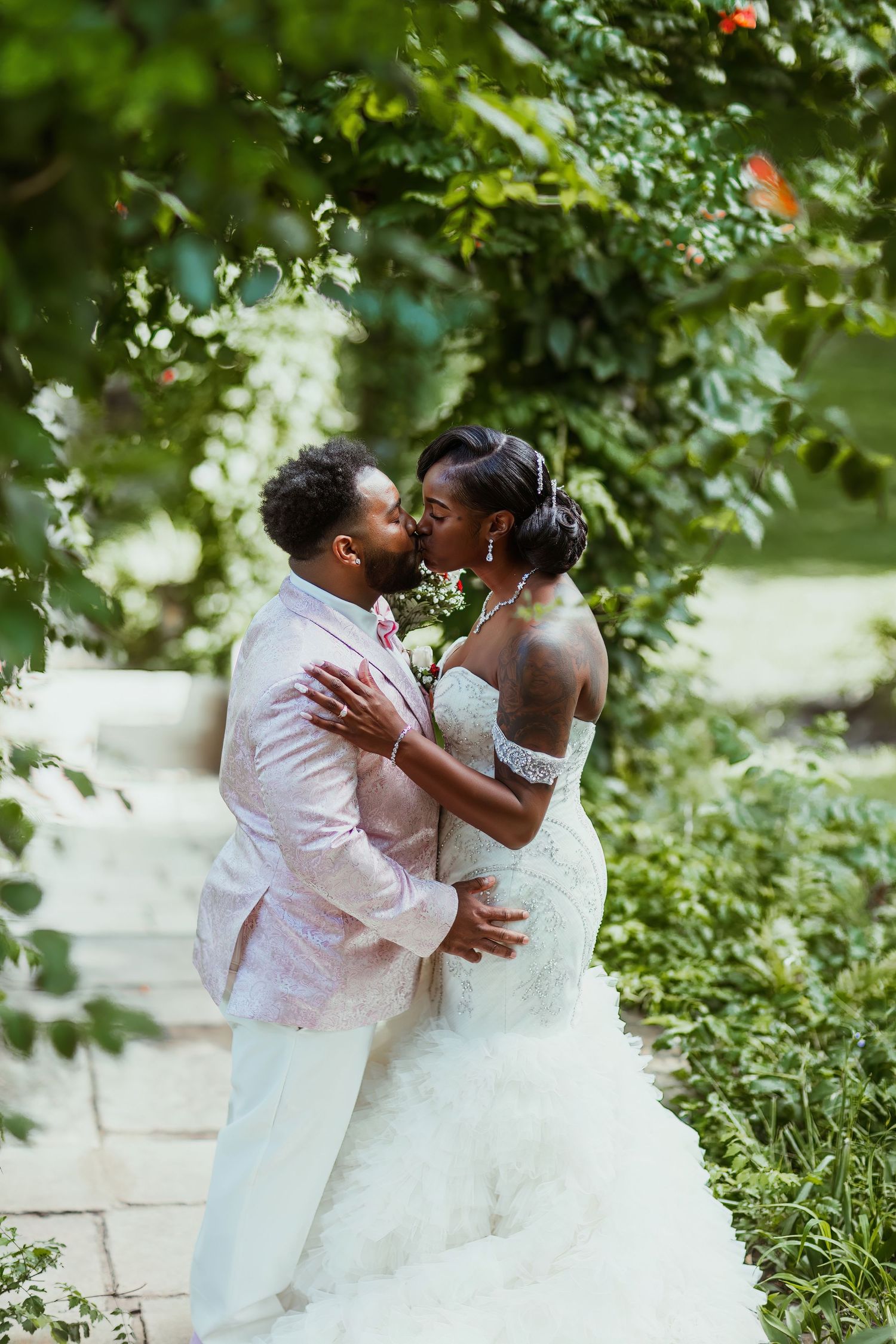 Romantic wedding couple shares intimate kiss in lush garden setting.