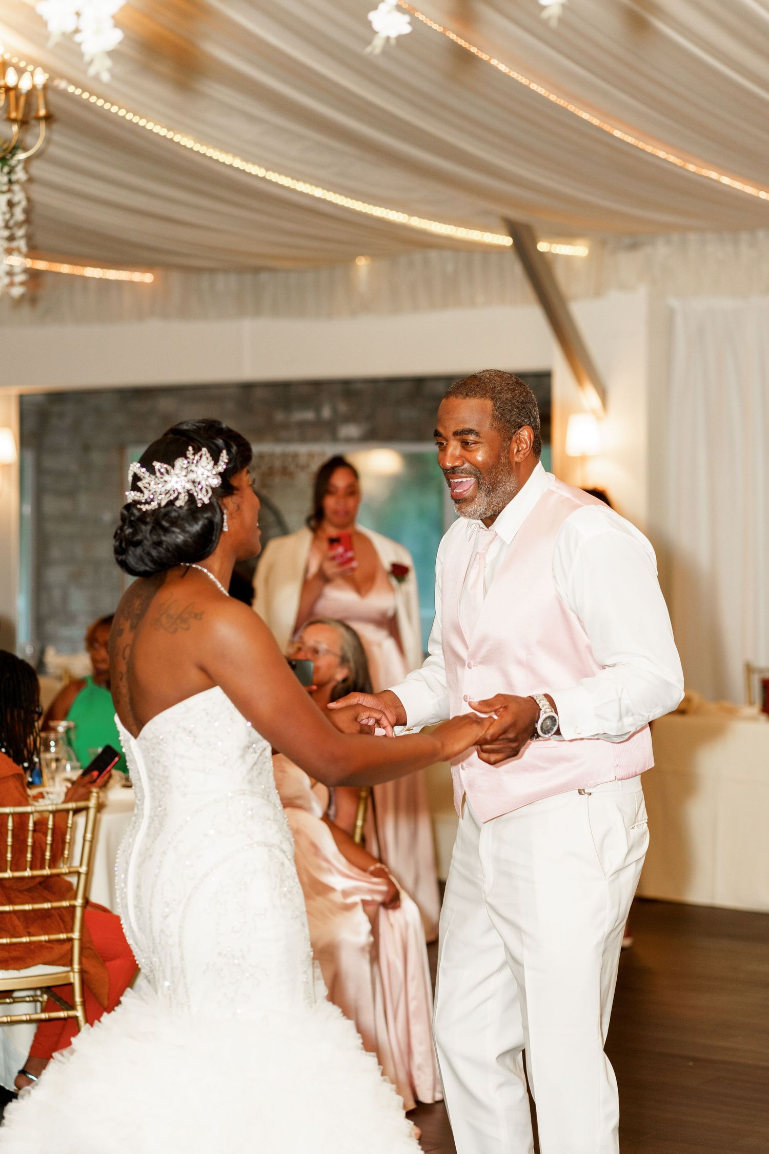 Wedding couple dancing under elegant draped ceiling with soft lighting and chandeliers.