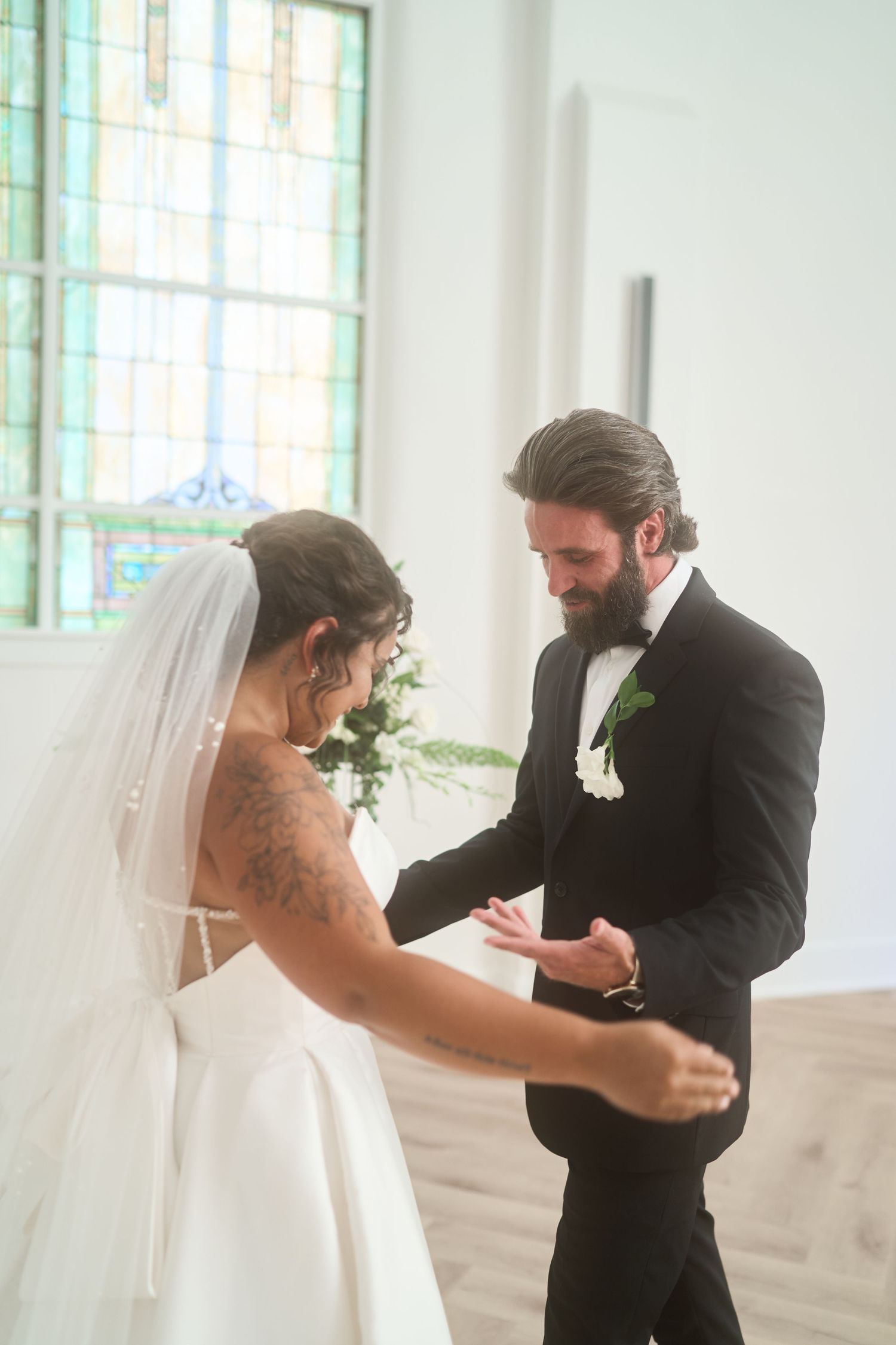 Bride and groom share tender moment during wedding first look in bright indoor venue.
