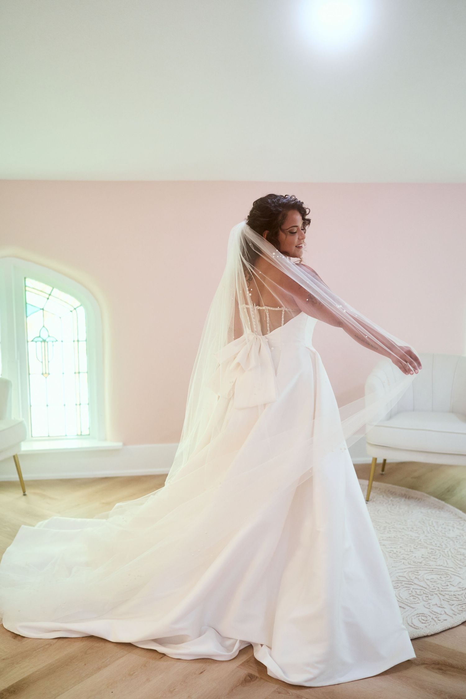 A figure twirls in an elegant white wedding dress with flowing veil in a sunlit room.