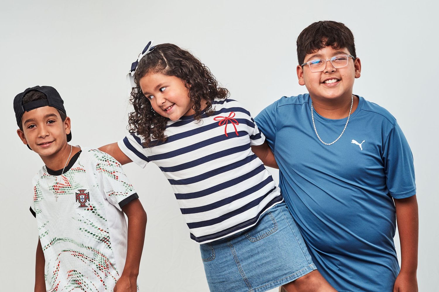 Three cheerful young teenagers in casual clothing lean together while posing against a white studio backdrop.