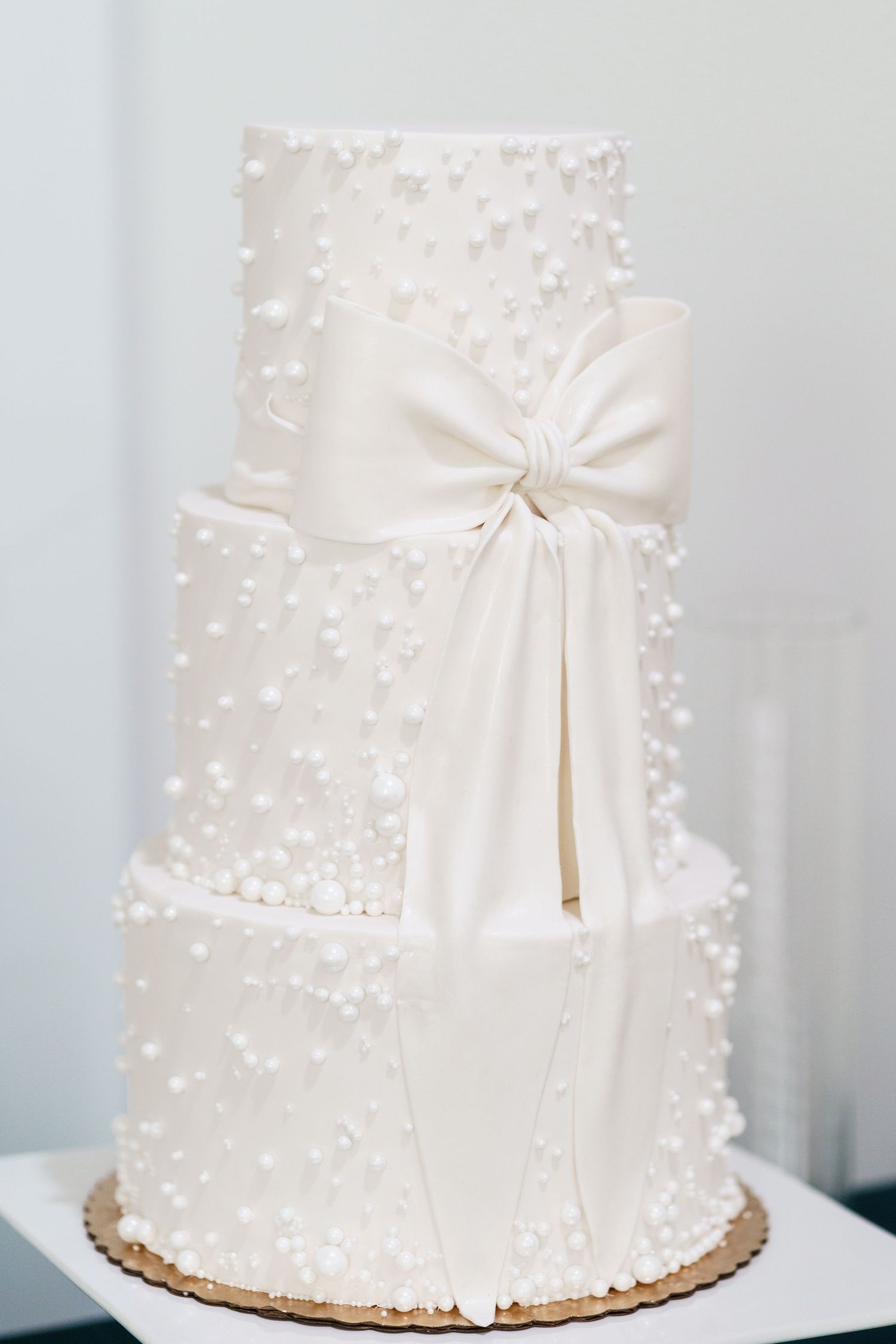 Elegant three-tier white wedding cake decorated with delicate pearl detailing and a large satin bow on the side.