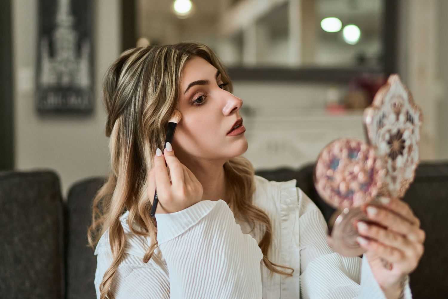 Woman in white turtleneck sweater sitting on couch holding phone and listening to music with wireless earbuds.