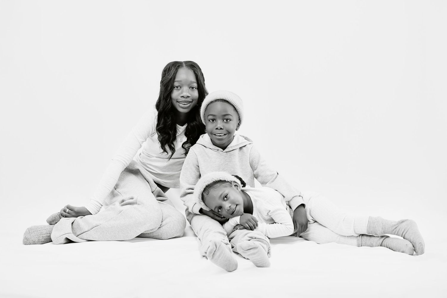 Family wearing white clothing lying together on white background in casual lifestyle portraits.