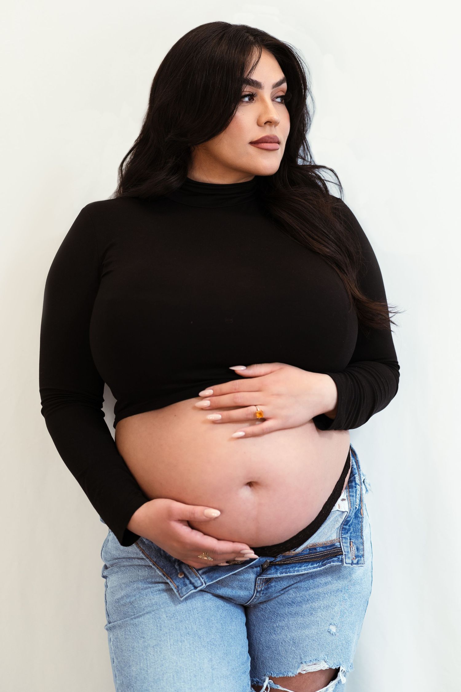 Four progressive photos show a person in a black sweater and jeans revealing their belly in different poses.