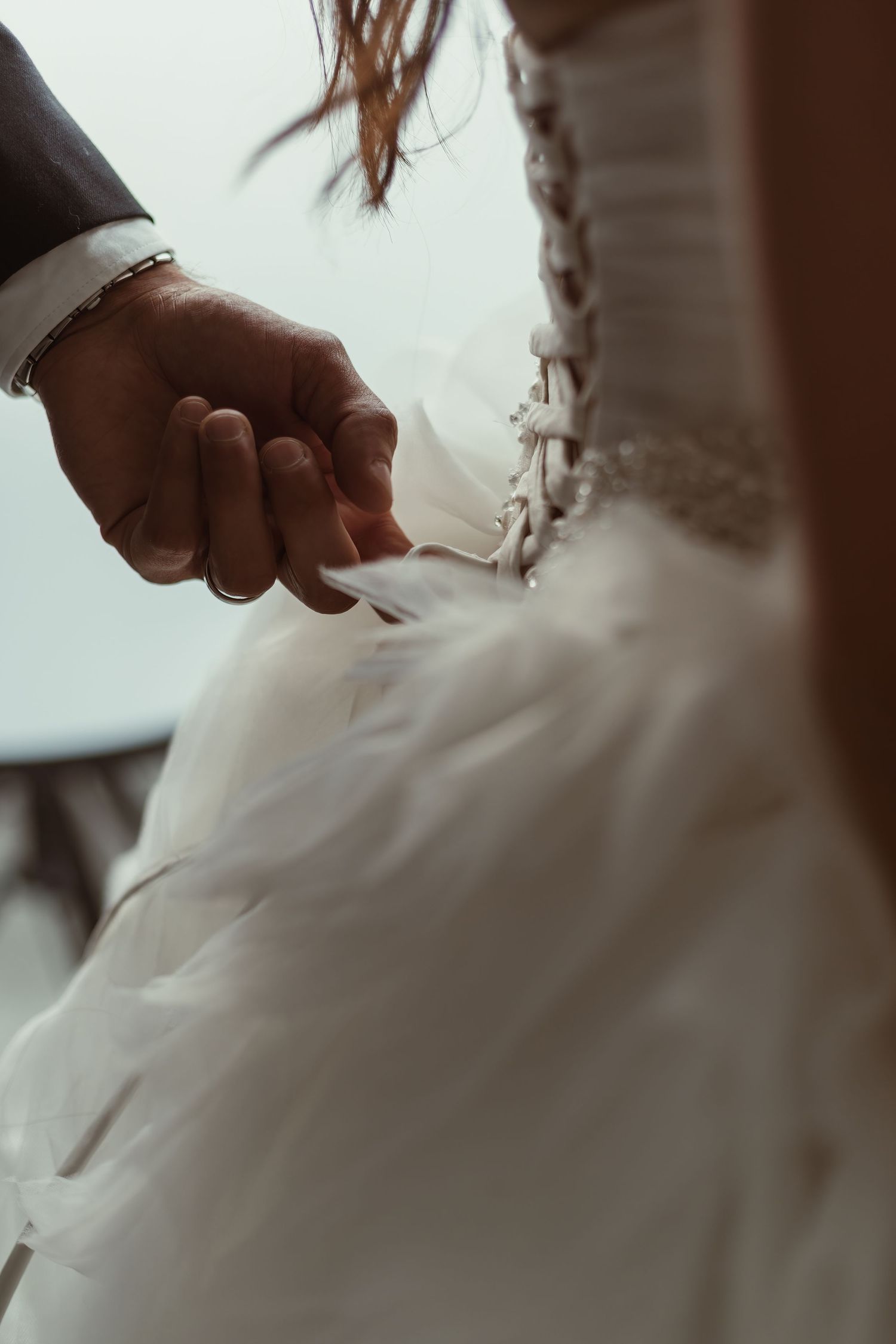 Close-up detail shot of hands adjusting corset back of wedding dress.