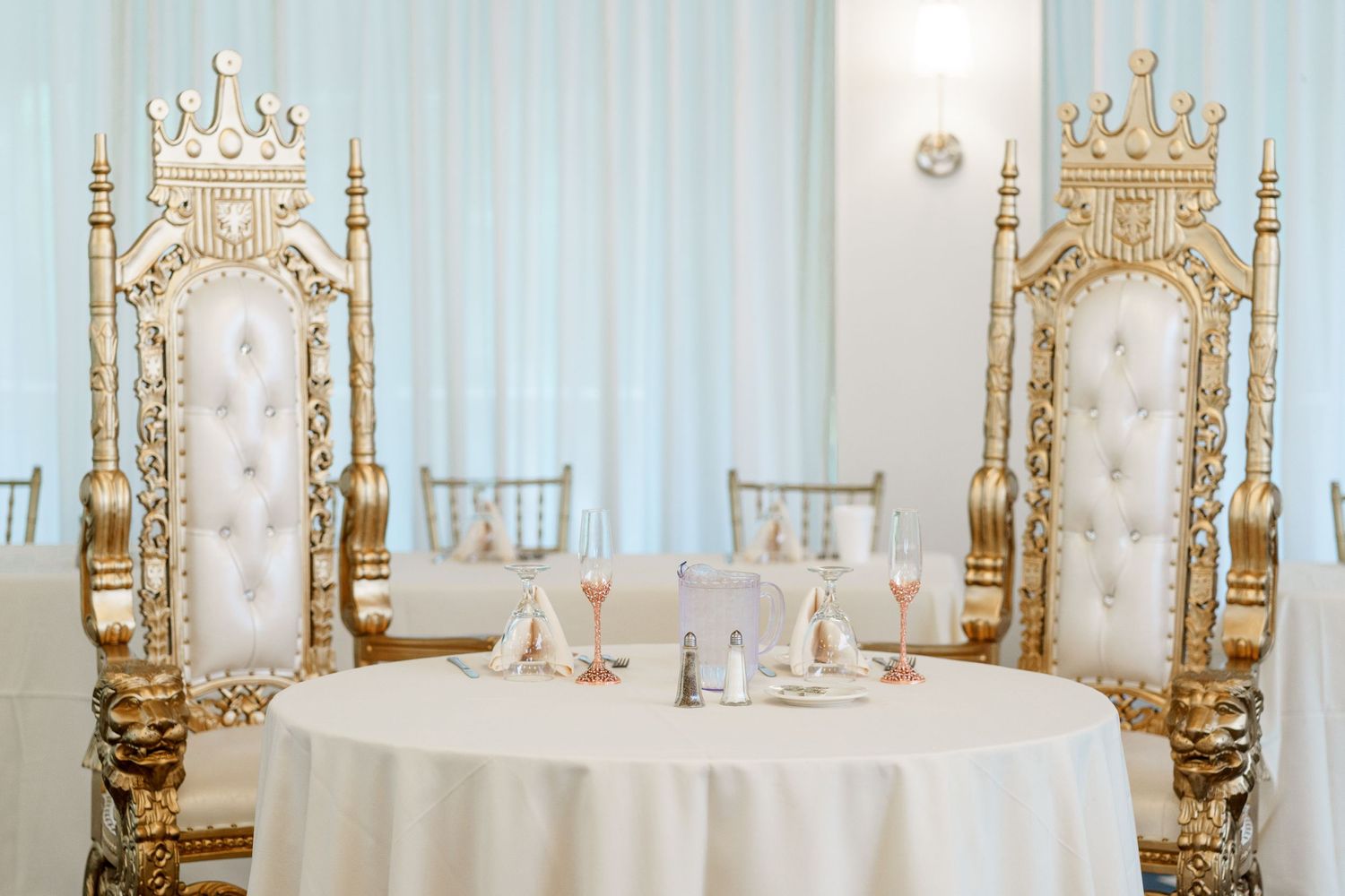 Elegant white and gold throne chairs at a wedding sweetheart table with place settings.