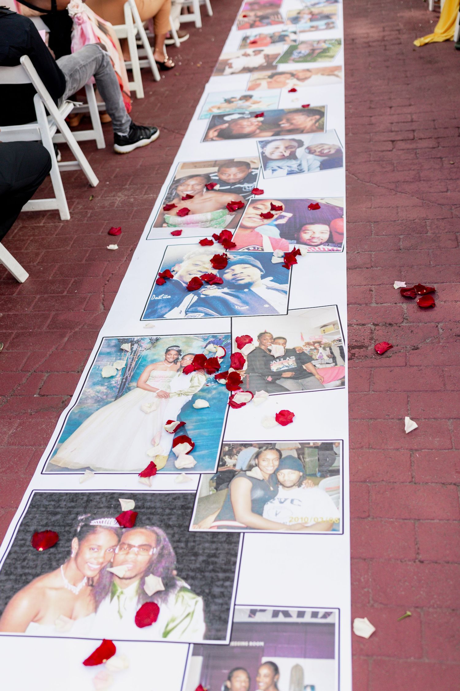A wedding aisle runner decorated with family photos and scattered red rose petals.
