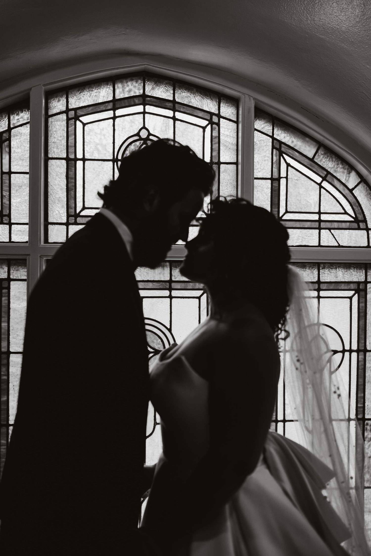 A dramatic black and white silhouette of a couple against a stained glass window backdrop.