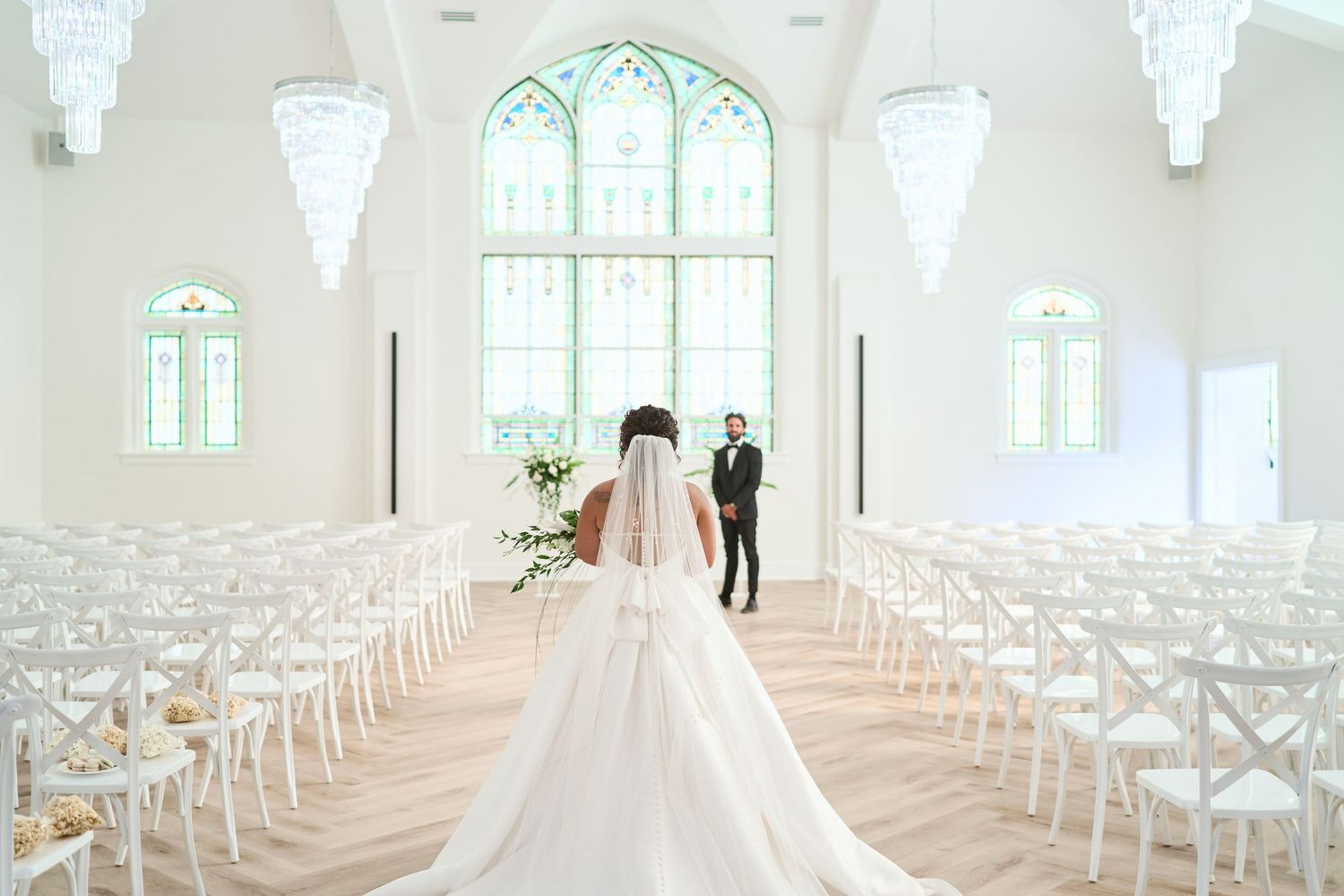 Wedding ceremony venue with white chairs leading to an arched window where a couple stands at the altar.