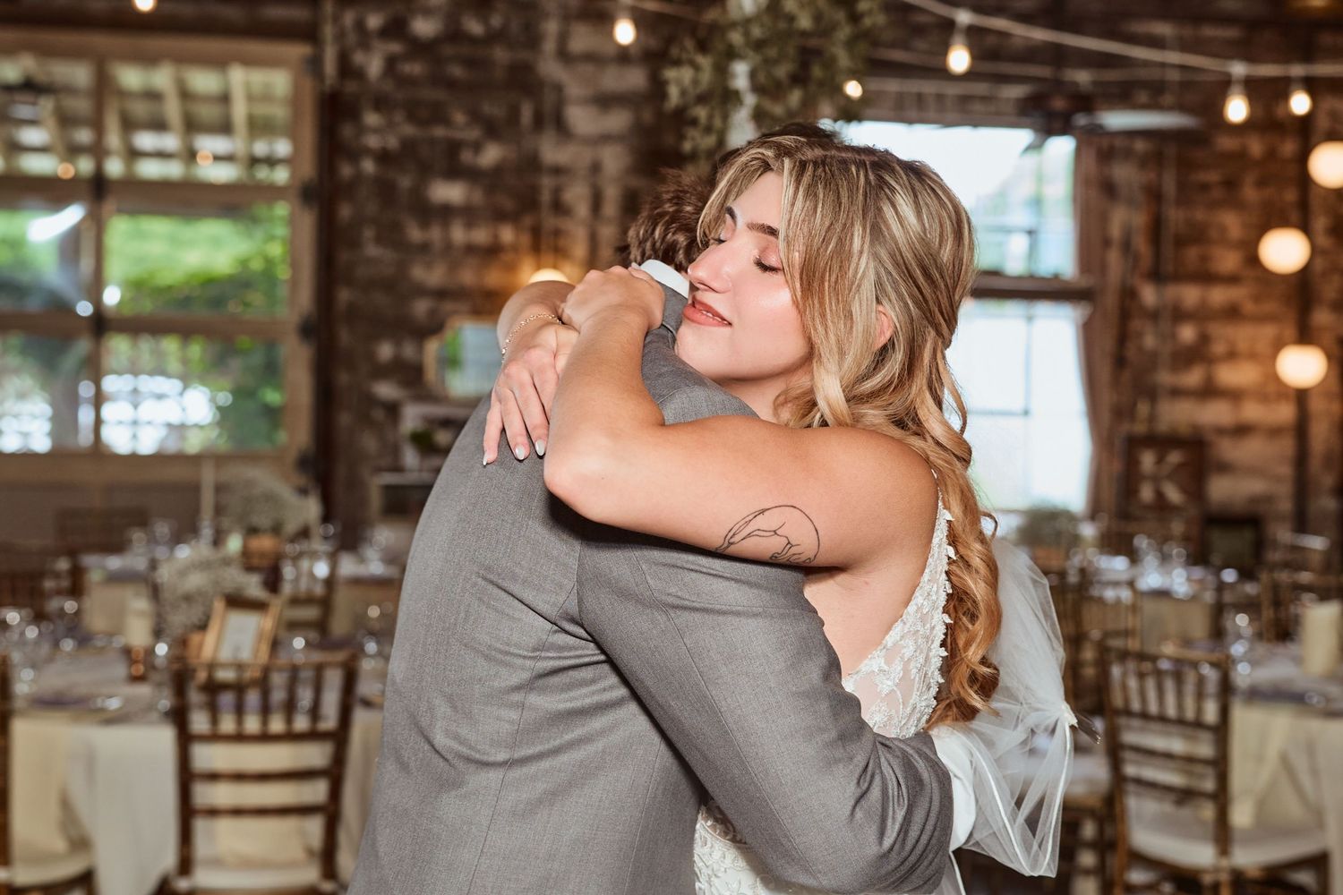 Wedding reception scene with string lights and rustic decor as guests share emotional embraces.