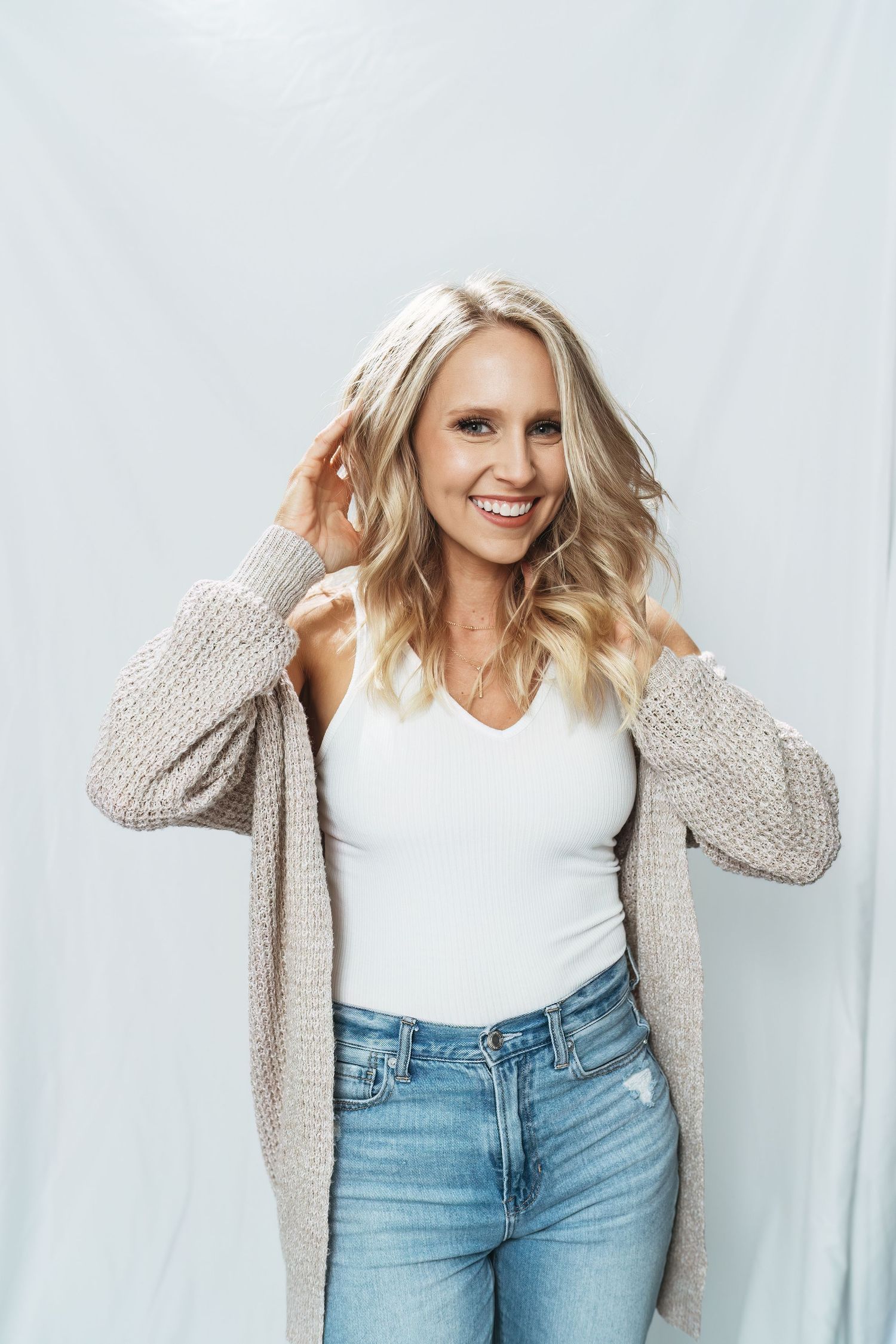 Casual lifestyle fashion photo series showing light beige cardigan styled with white top and light wash denim jeans.