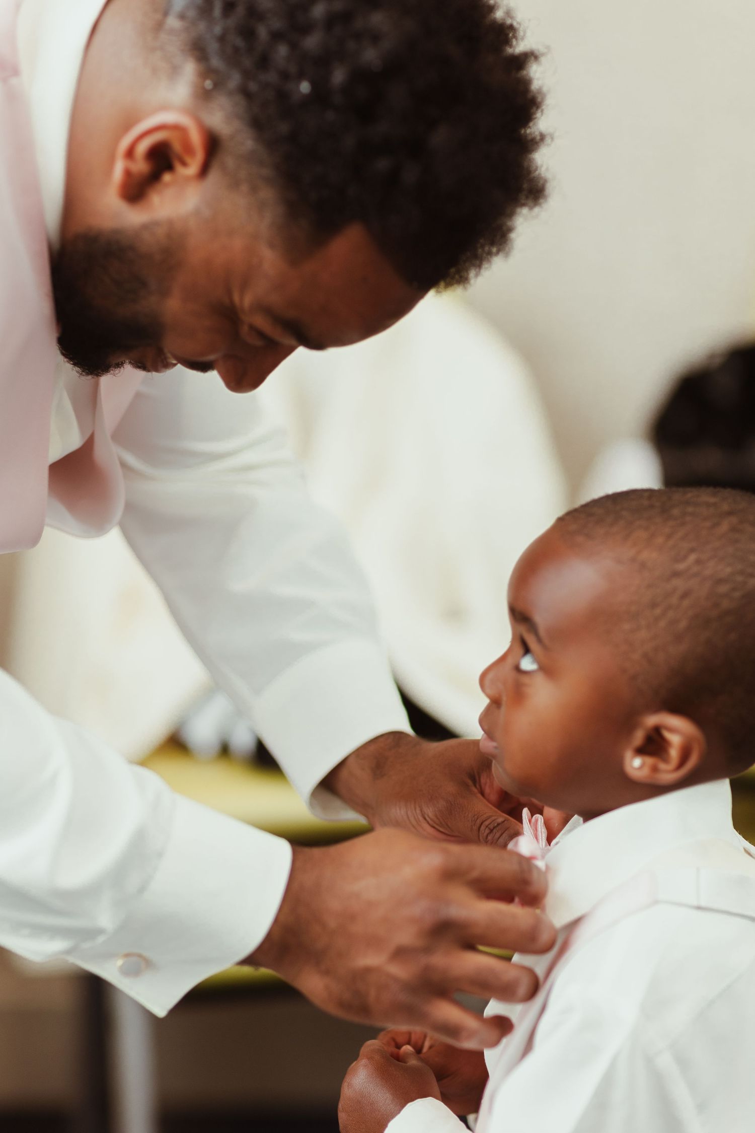 Close-up of adult helping child with formal white collar and tie.