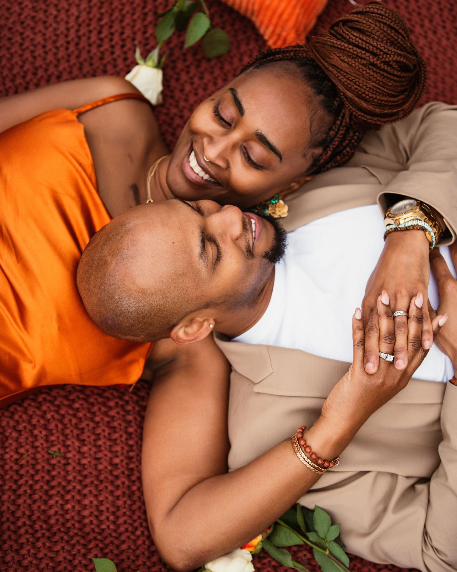 Couple in orange and beige outfits sharing an intimate moment on a red blanket.