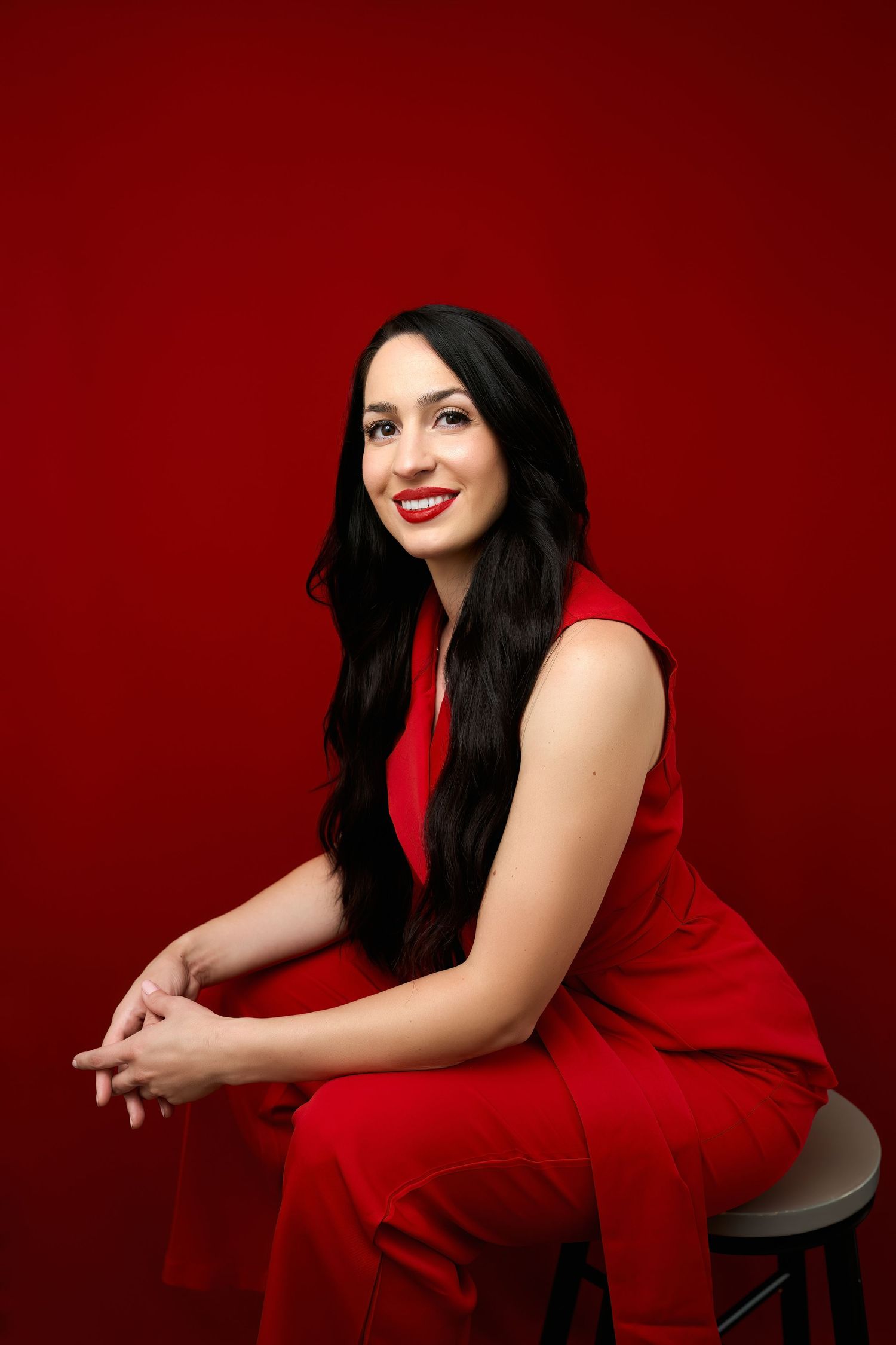 Portrait photo of someone in a vibrant red outfit seated against a deep red background, showcasing an elegant pose.