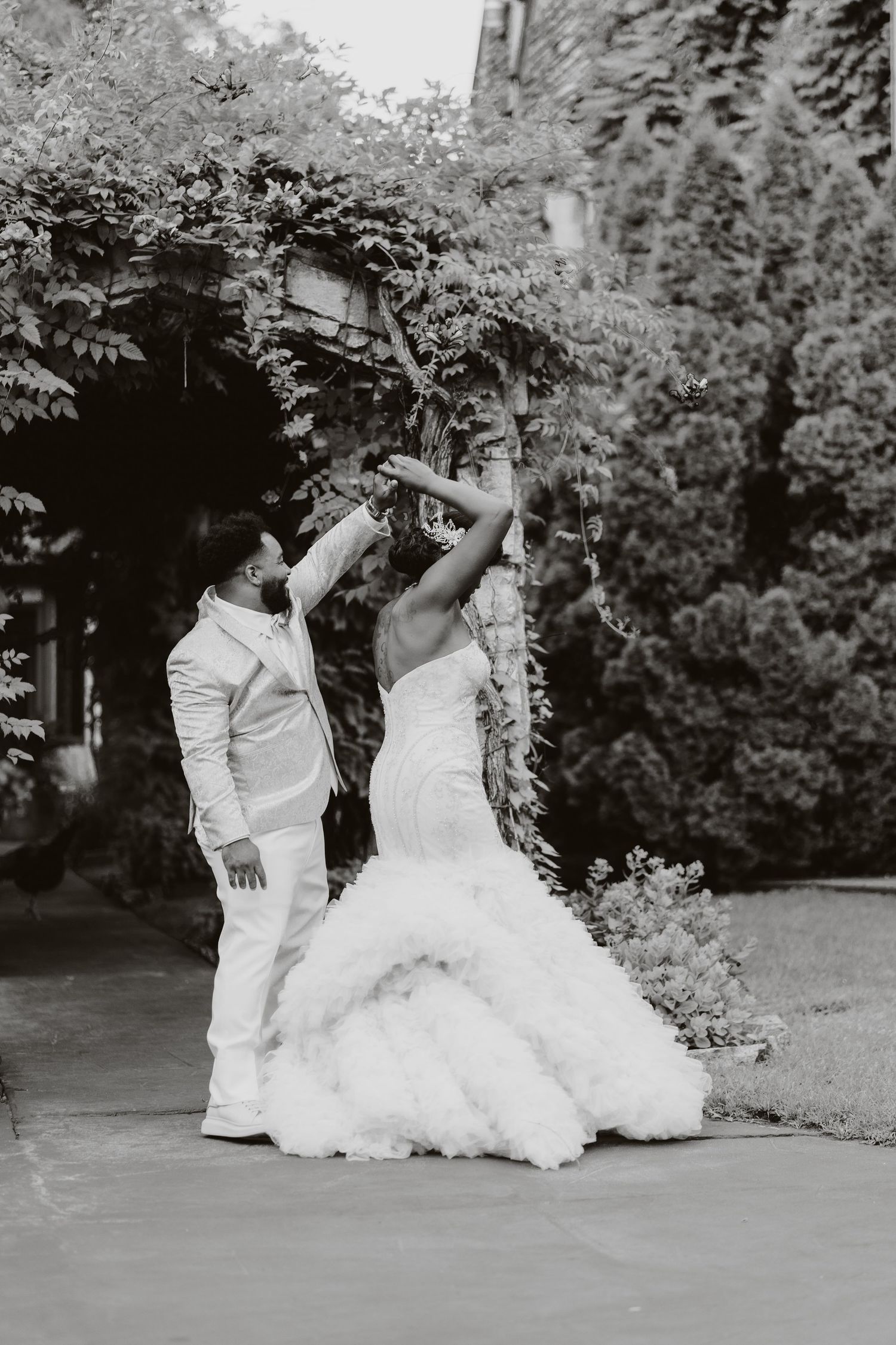 A black and white photo of a couple dancing in an elegant garden setting.