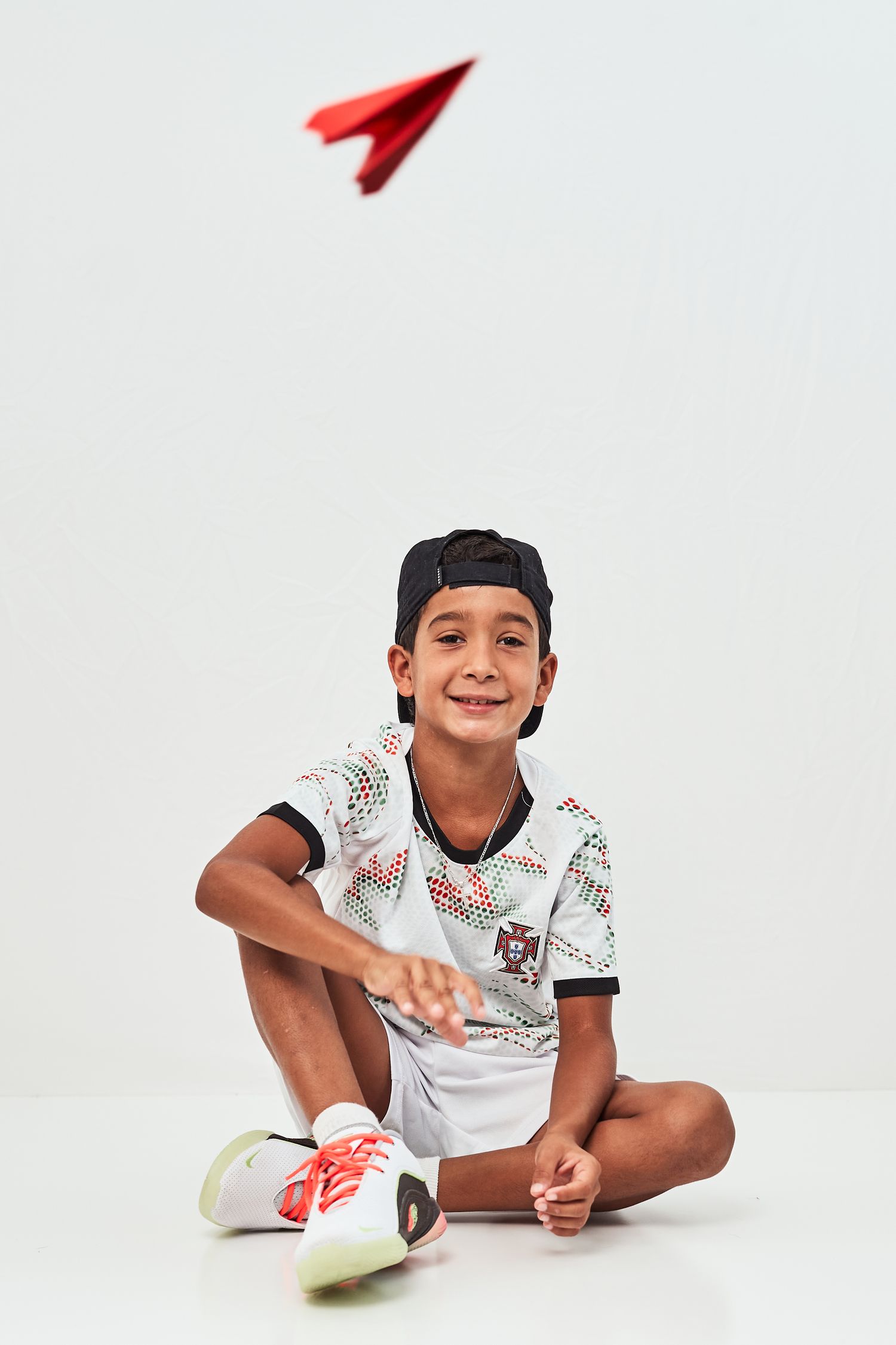 A child in a white patterned shirt lies on their side on a white background, smiling at the camera.