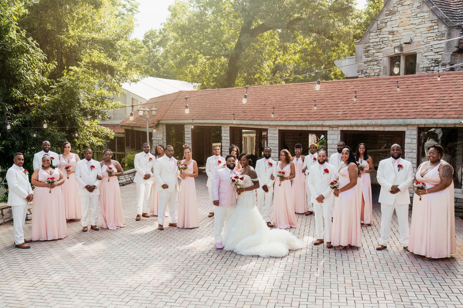 Wedding party in pink and white dresses poses elegantly on a stone patio during sunset.