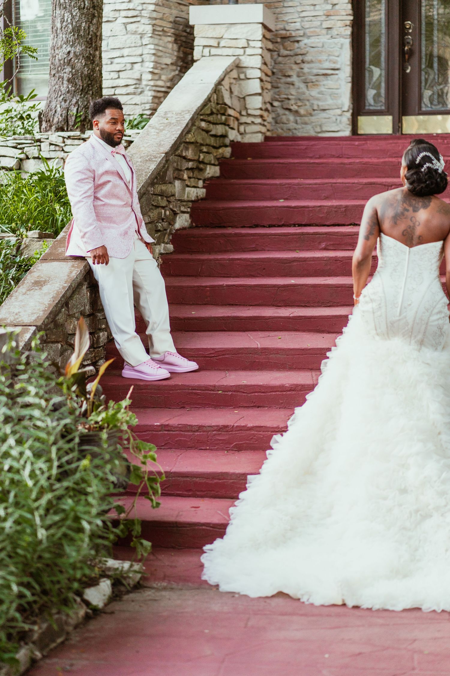 A wedding couple poses on red painted steps against a stone building.