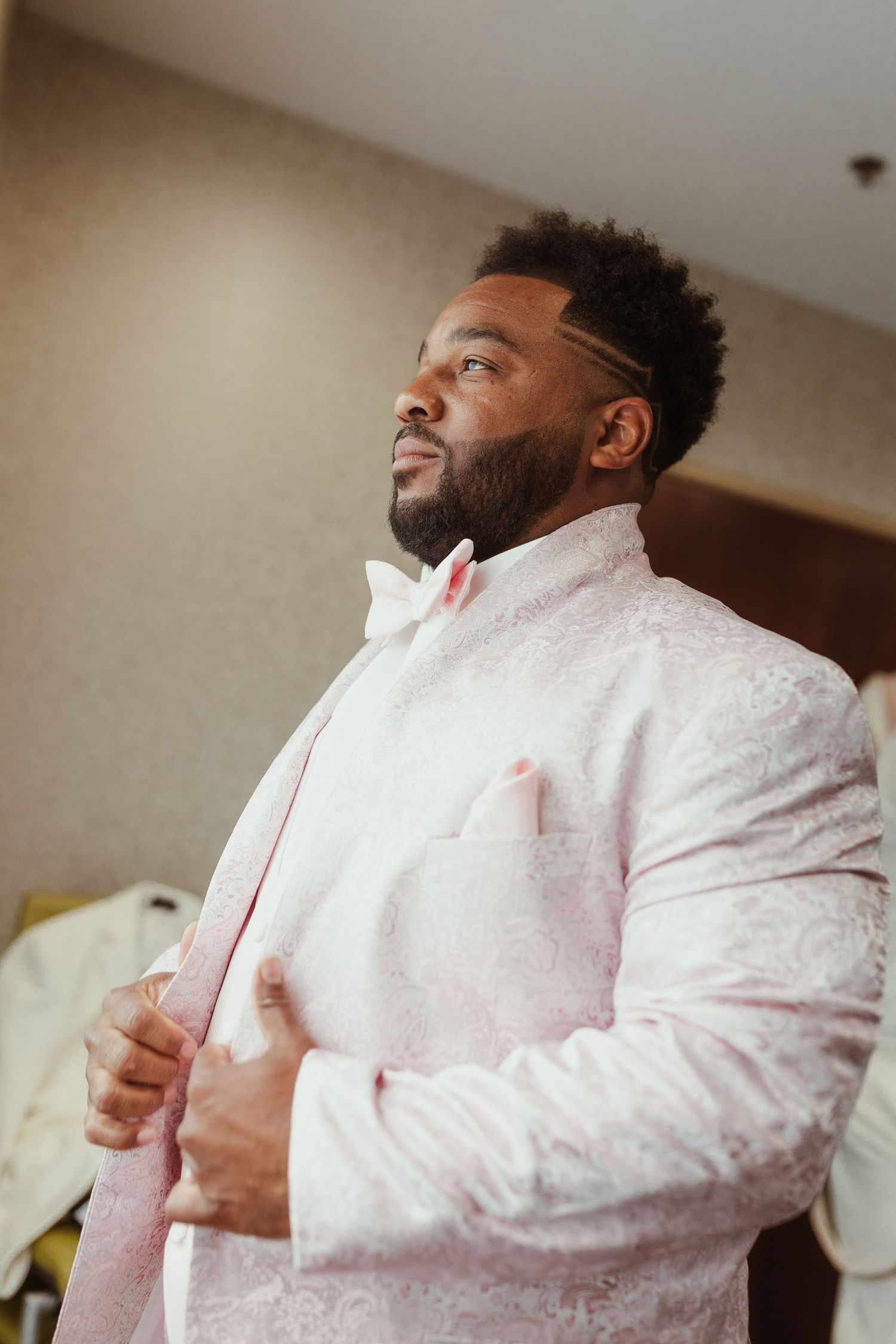 Person in a white embroidered formal jacket with a pink bowtie adjusting their attire.