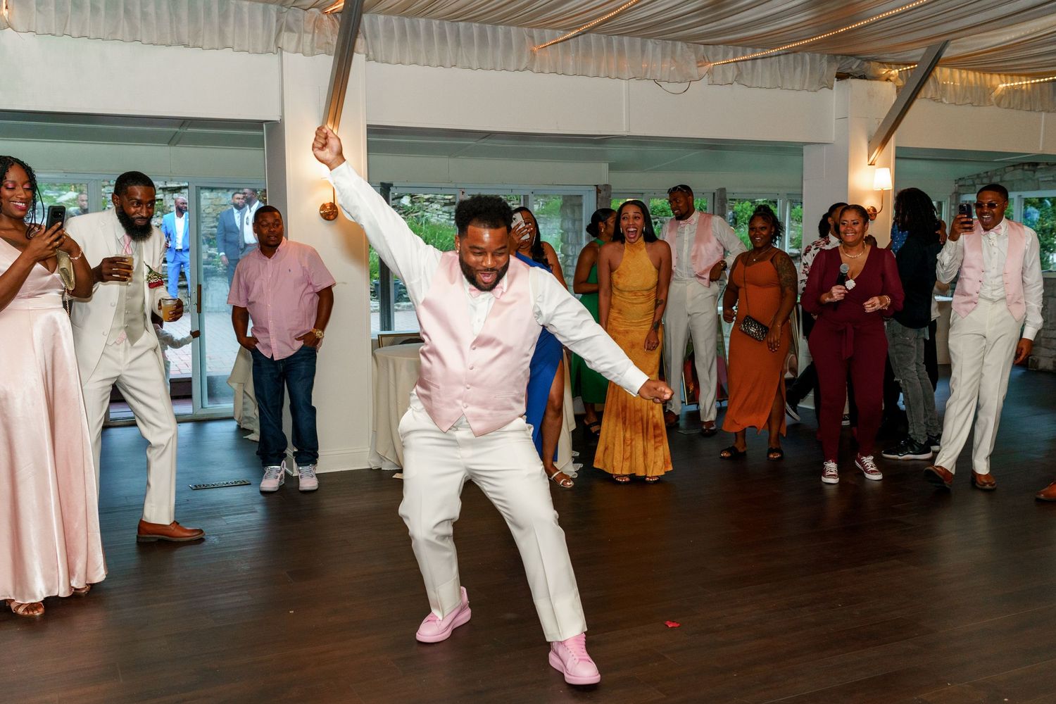 Energetic guest performs solo dance moves at wedding reception under draped ceiling and chandeliers.