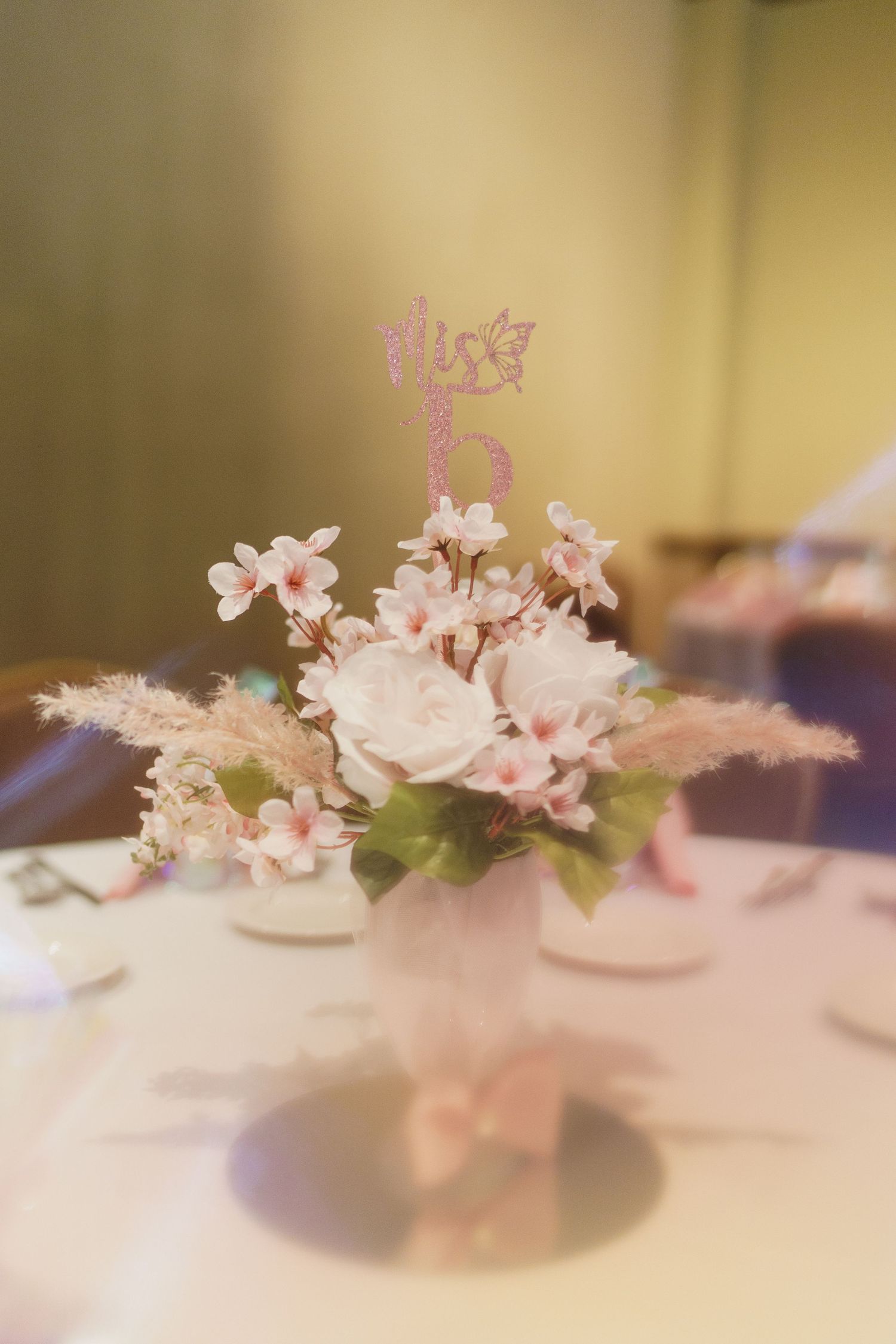 Delicate pink floral centerpiece arrangement with roses and small flowers on a table setting.