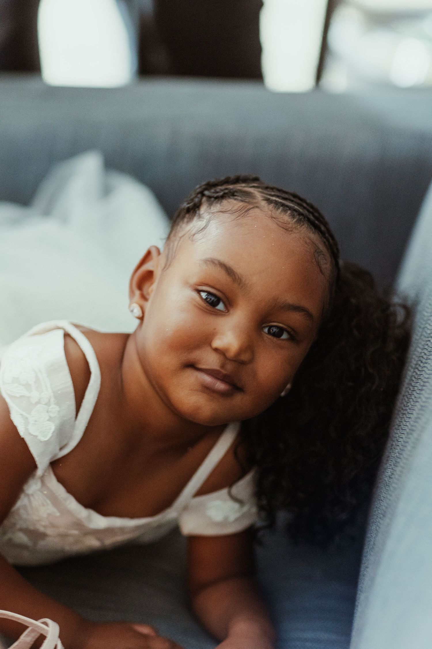 Young child in white top smiling while relaxing on couch with natural lighting.