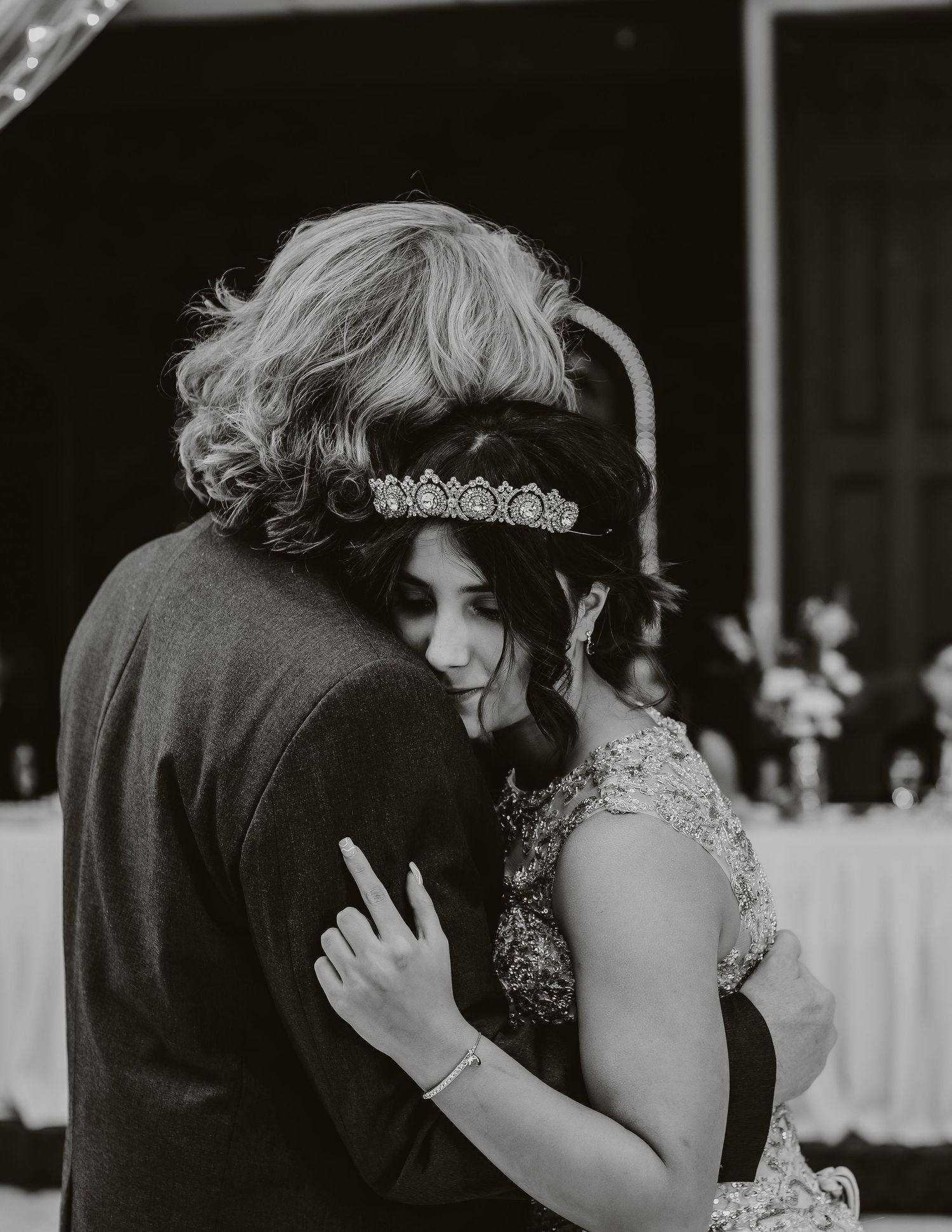 A black and white intimate moment captured during a wedding dance under crystal chandeliers.