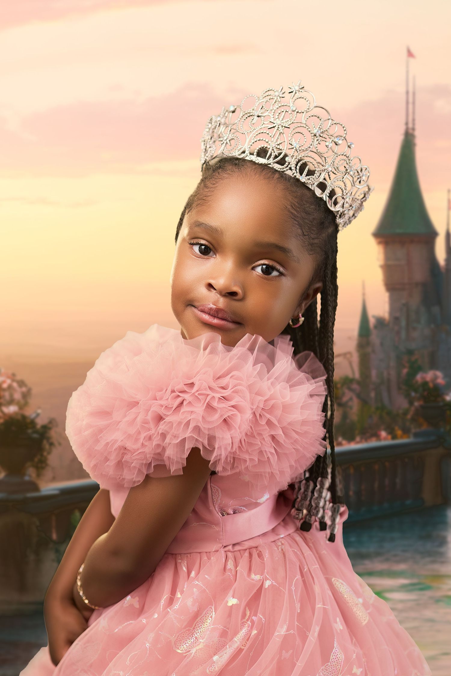 Portrait in a pink tulle dress with a crown posing against a fantasy castle backdrop at sunset.