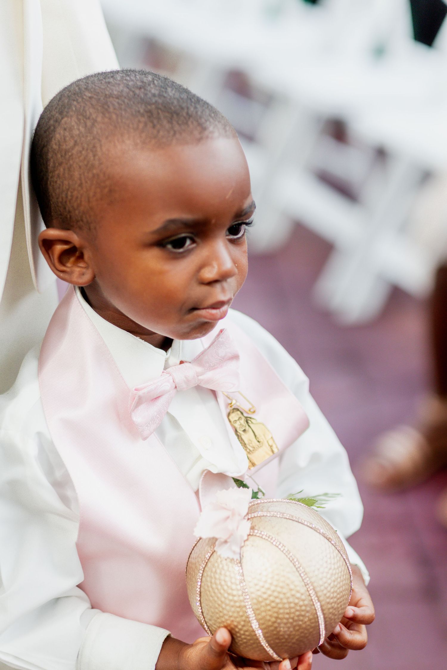 Young ring bearer in pink vest and bowtie holds golden ceremonial sphere.