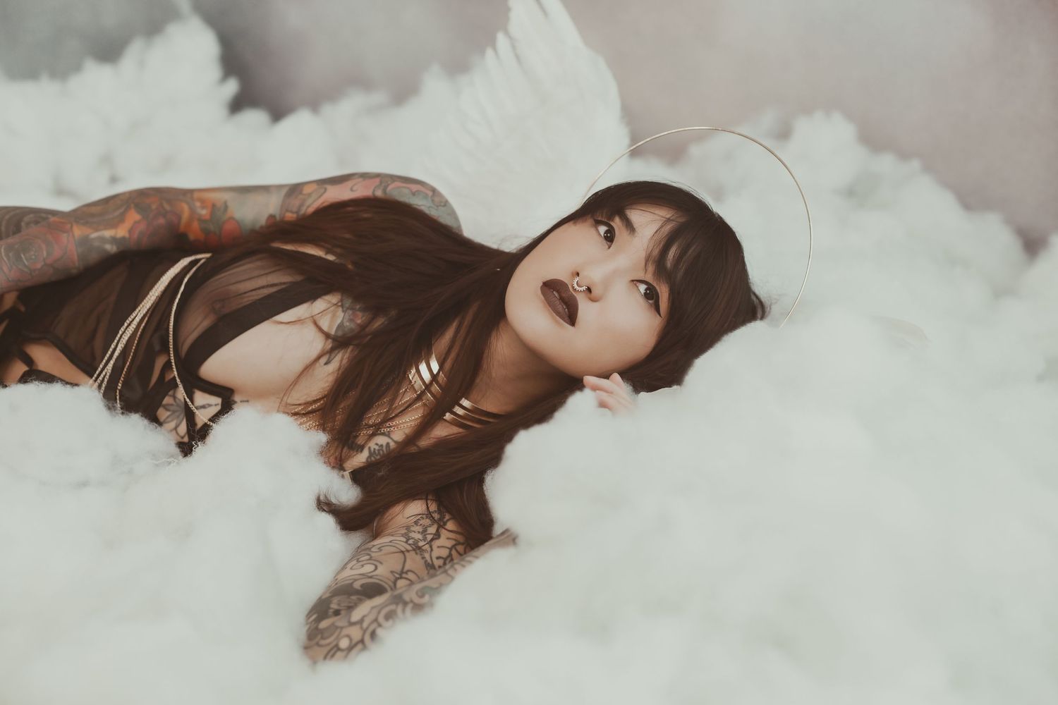 A sensual portrait of a model with tattoos lying among ethereal white clouds.