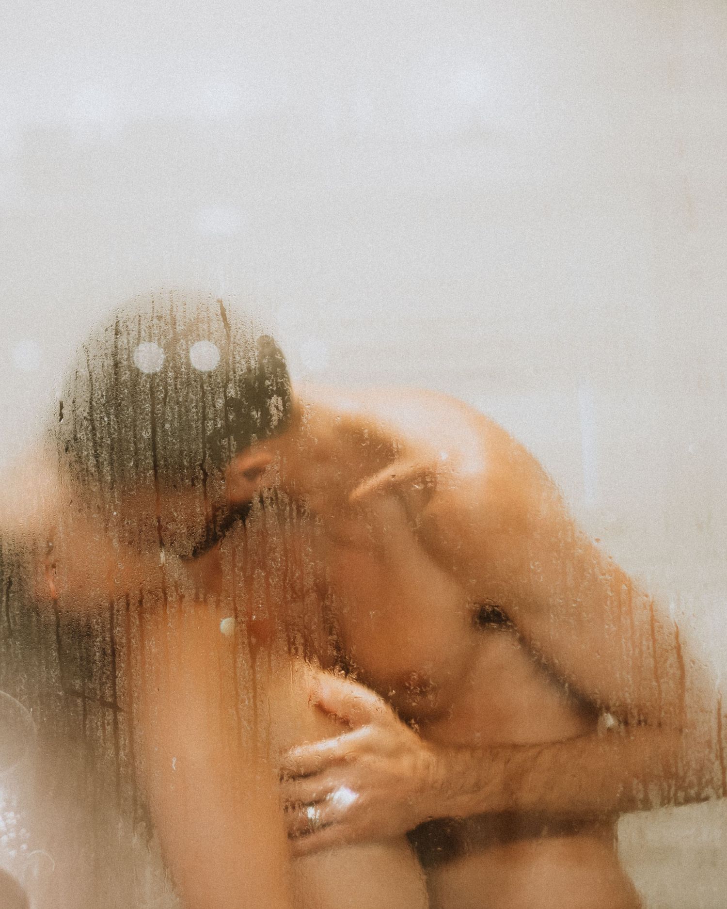 Intimate silhouettes visible through steamed glass with water droplets.