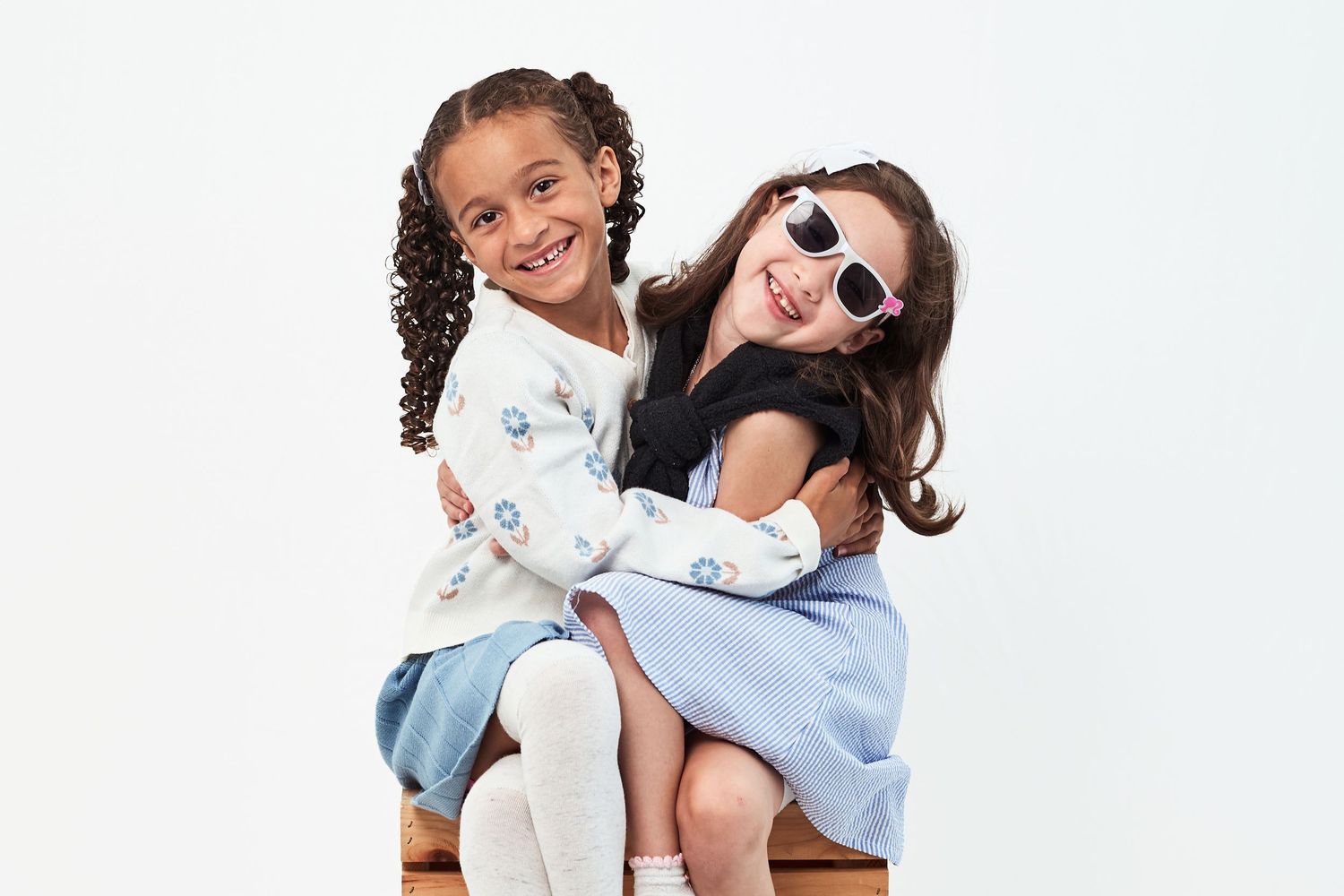 Two smiling children hugging and posing together against a white background.
