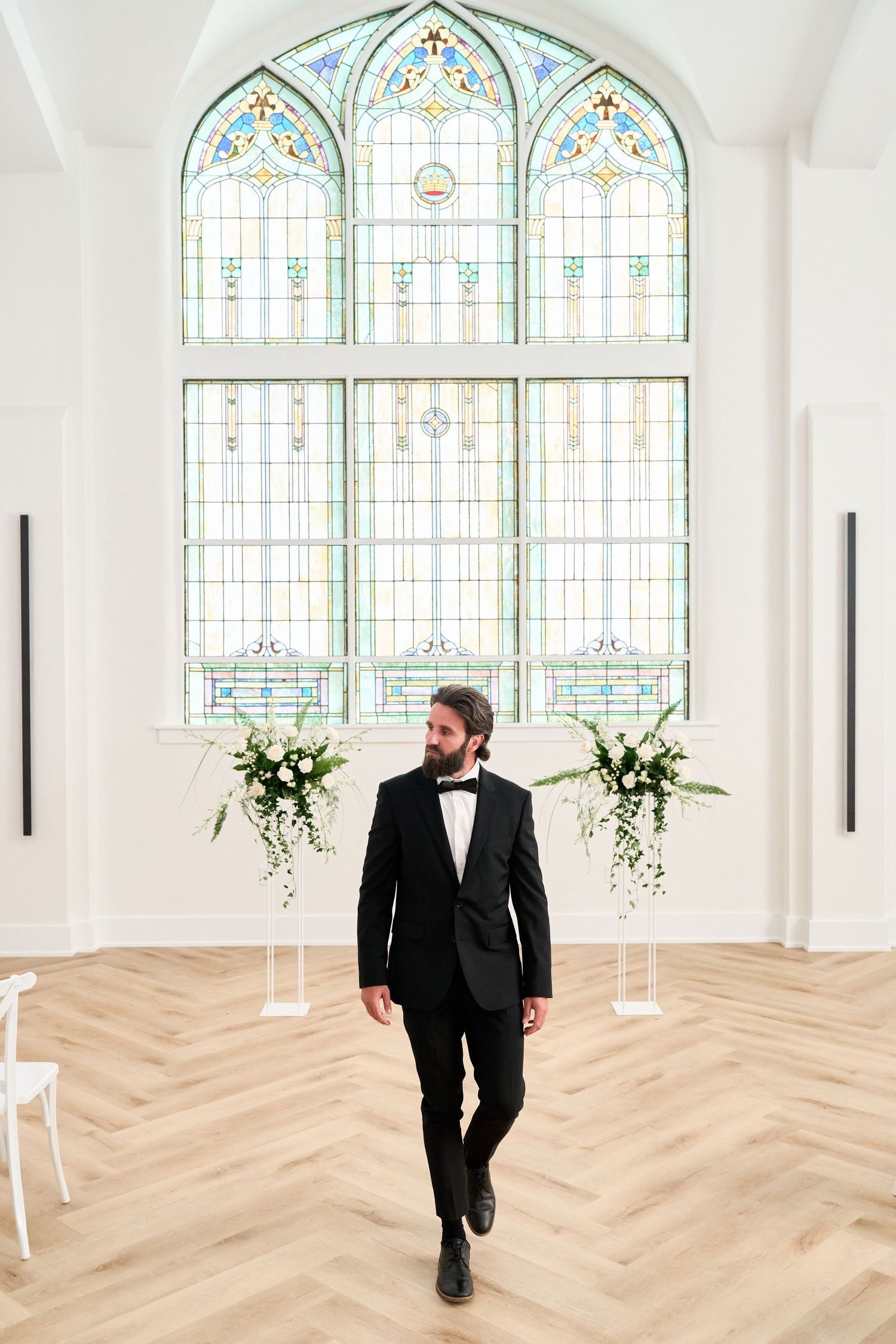Stained glass church window with elegant floral arrangements and herringbone wood flooring.