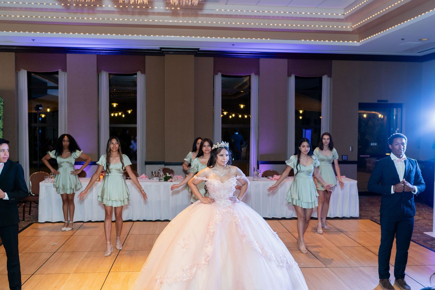 A group dances in an elegant ballroom during a celebration featuring a voluminous white ball gown and mint green dresses.