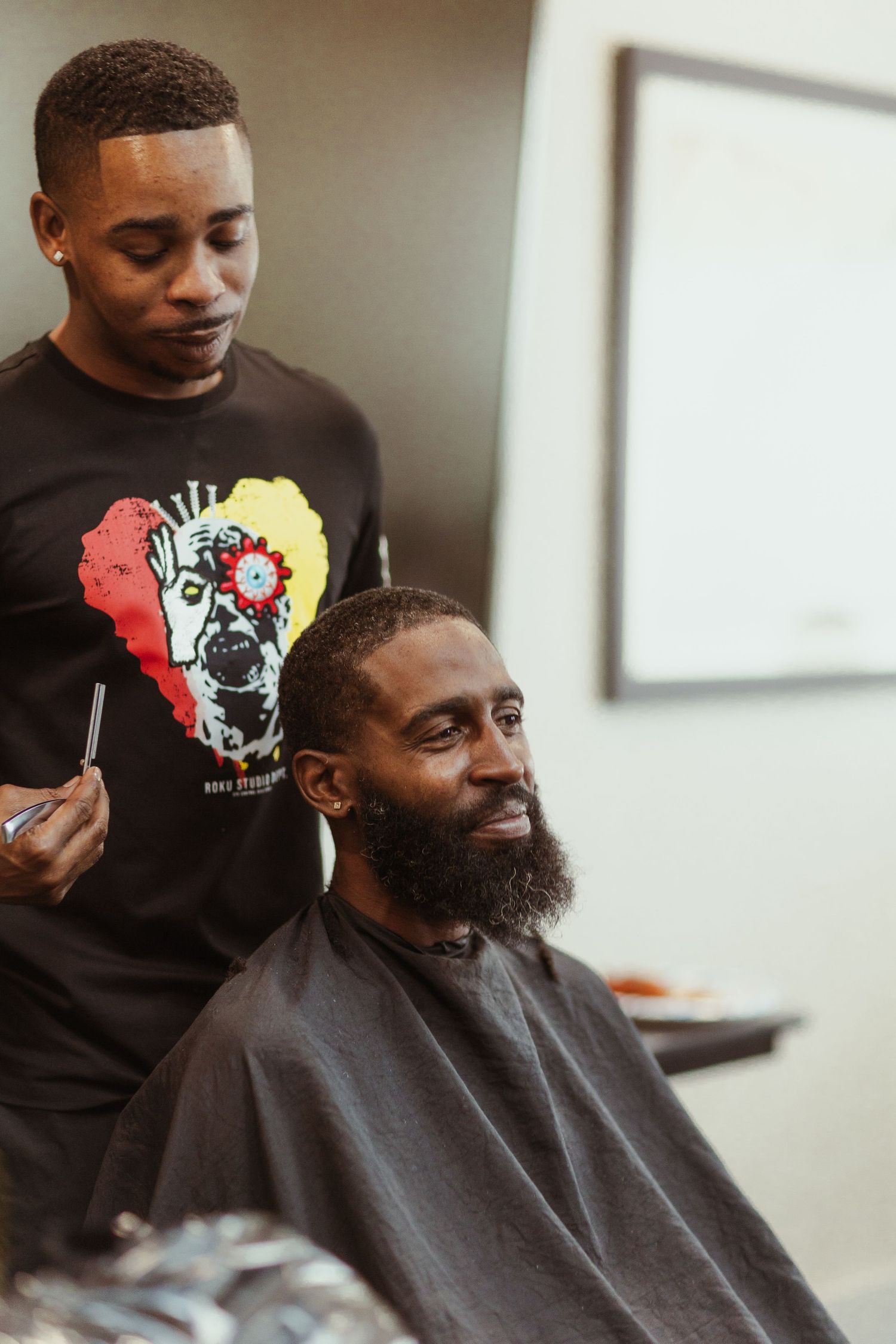 Barber wearing colorful skull t-shirt giving haircut to client in salon chair.