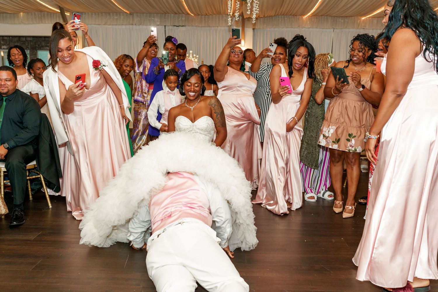 Lively dance celebration at wedding reception with guests in pink dresses cheering.