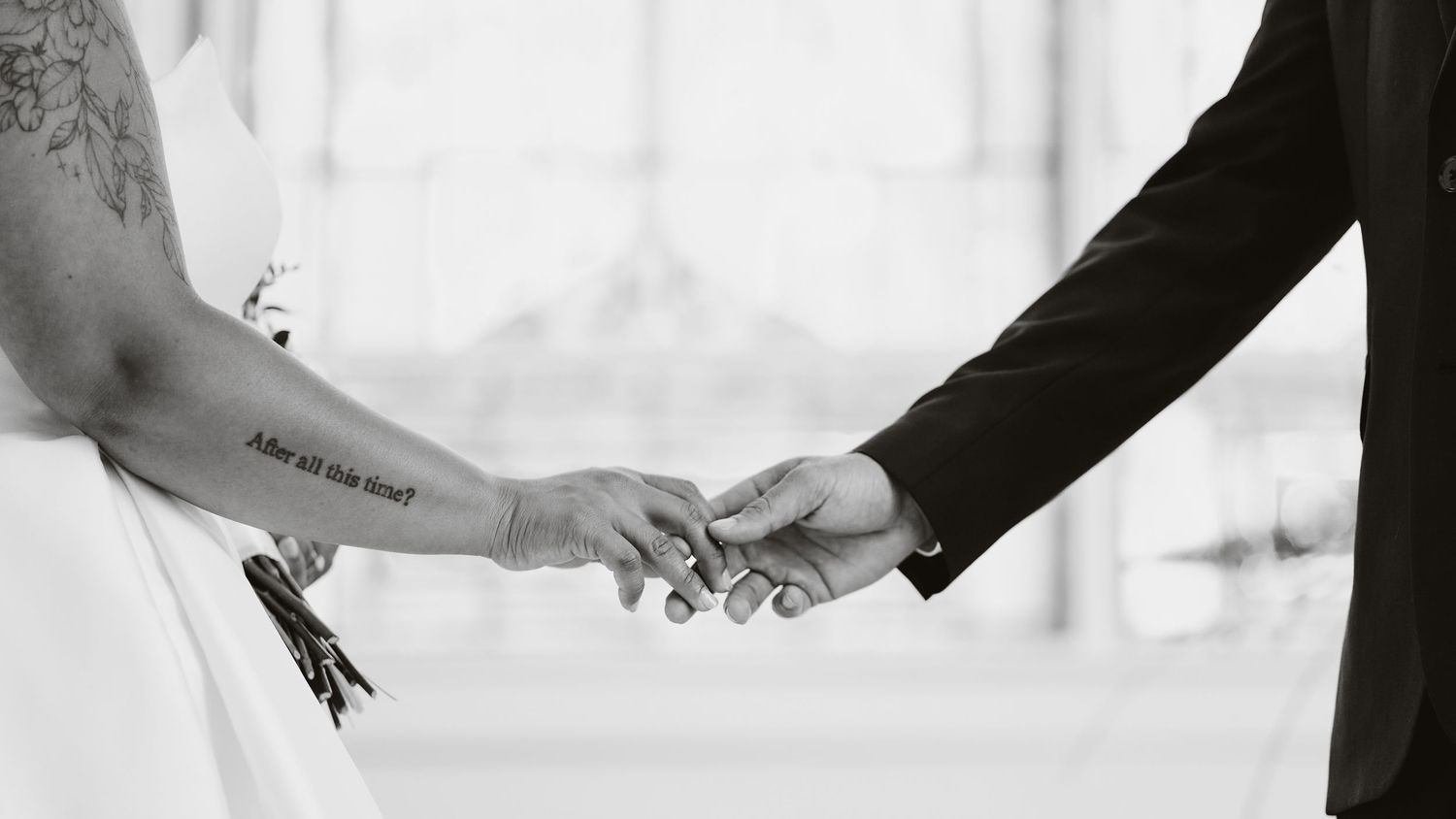 Two hands reaching towards each other in black and white, one wearing a wedding dress sleeve and the other in a suit jacket.