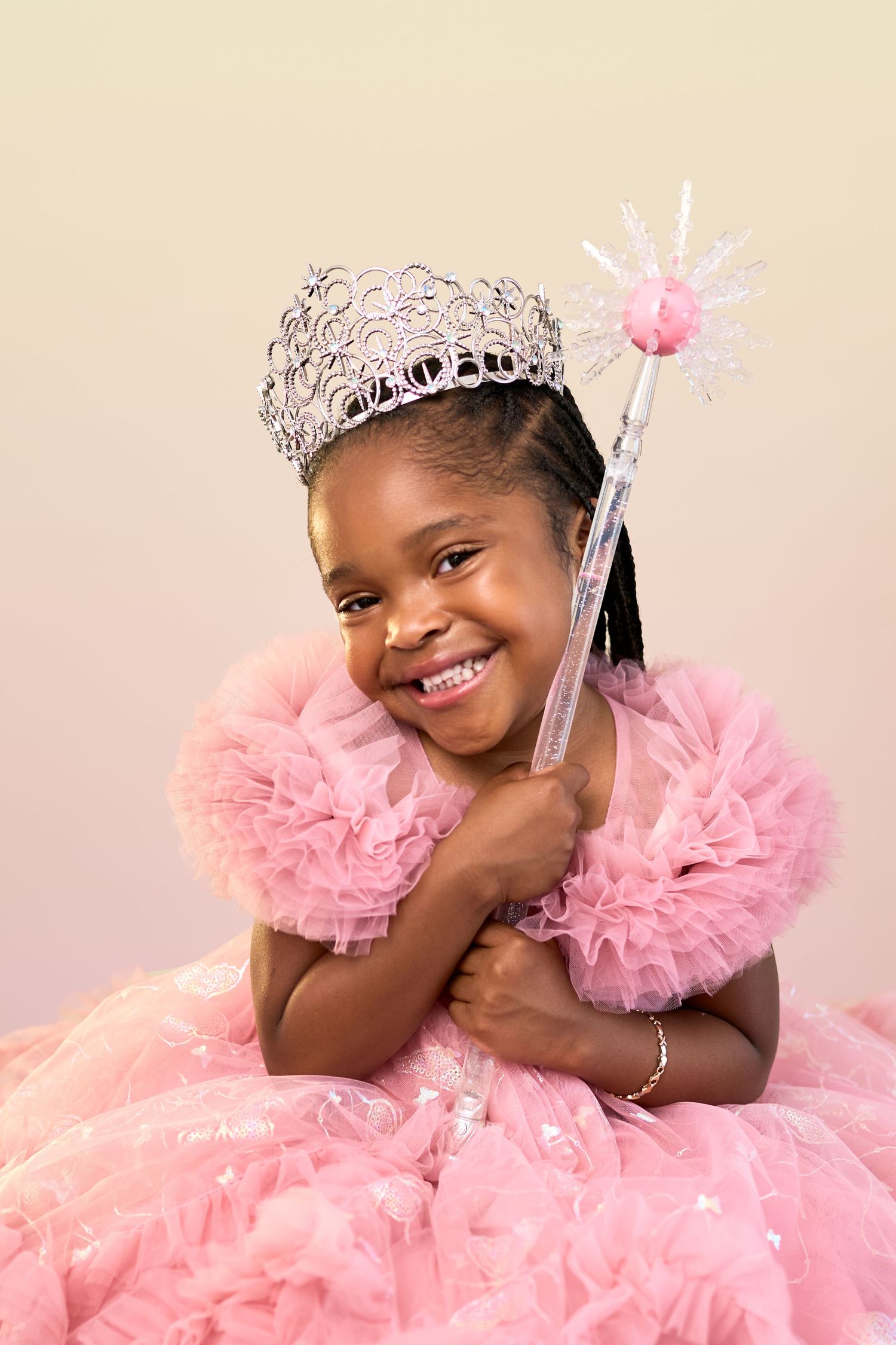 A joyful child wearing a silver tiara and pink tulle dress poses in varying happy expressions for a photoshoot.