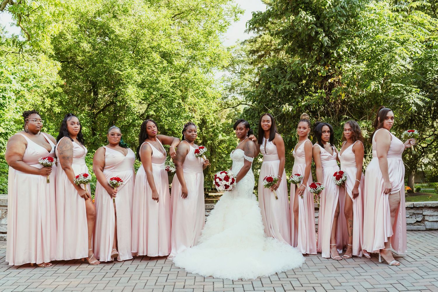 Wedding party in blush pink dresses and white gown stands together in a garden setting.