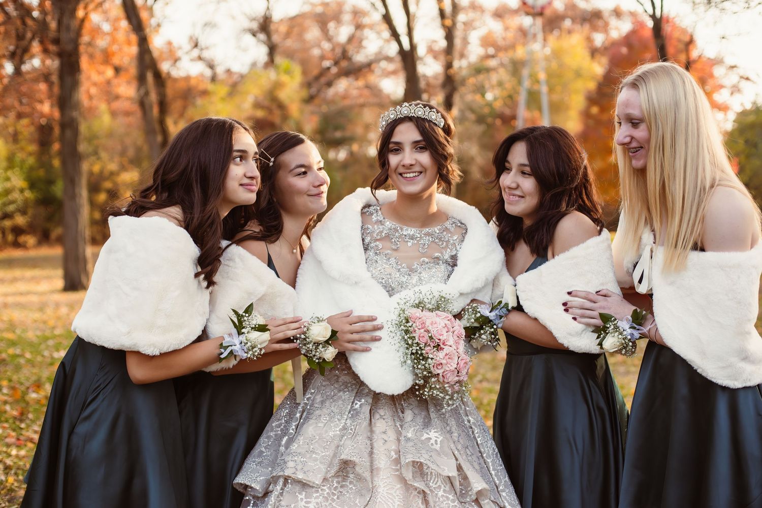 Bridal party in navy dresses and white fur wraps sharing moment in fall setting.
