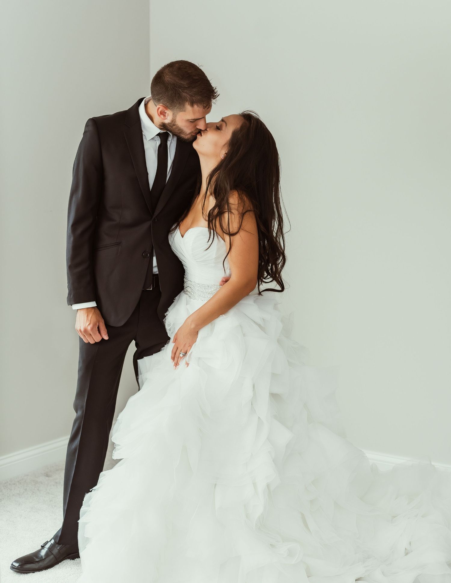 A romantic wedding photo of a couple sharing an intimate moment in formal attire against a light gray backdrop.
